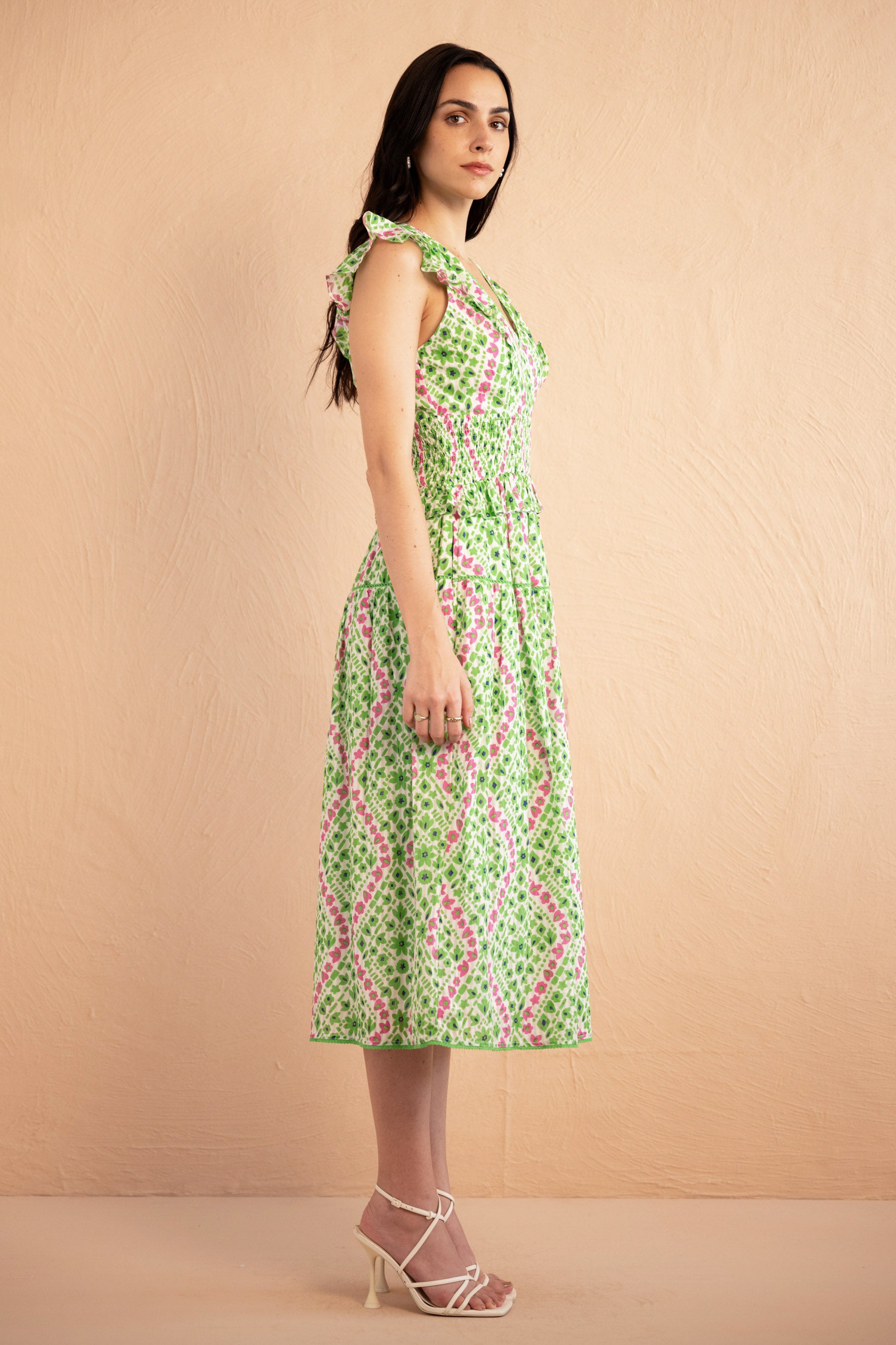 Side view of the Keira dress in a fresh green and pink Athena Heart print with floral and heart motifs. The dress features lace trim along the neckline and sleeves, a smocked waist for a flattering fit, and soft frill accents. The A-line skirt falls to the shin, and the dress includes discreet side pockets.