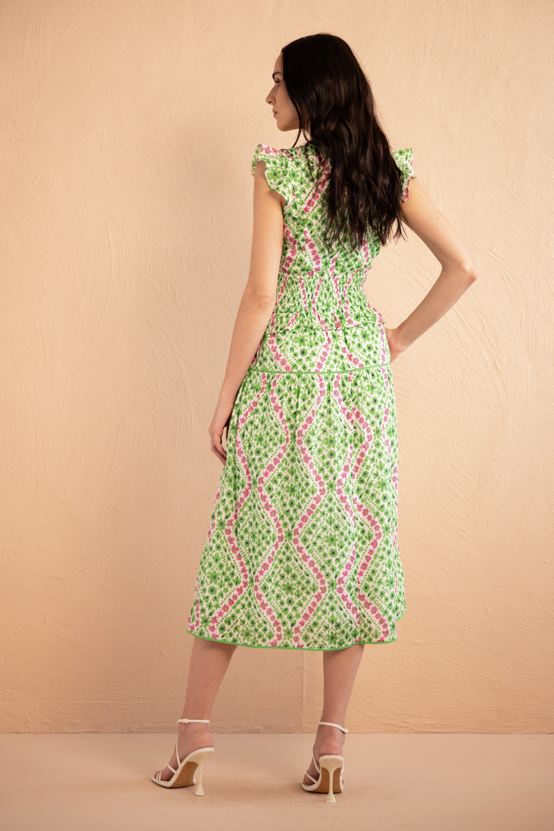 Back view of the Keira dress in a fresh green and pink Athena Heart print with floral and heart motifs. The dress features lace trim along the neckline and sleeves, a smocked waist for a flattering fit, and soft frill accents. The A-line skirt falls to the shin, and the dress includes discreet side pockets.