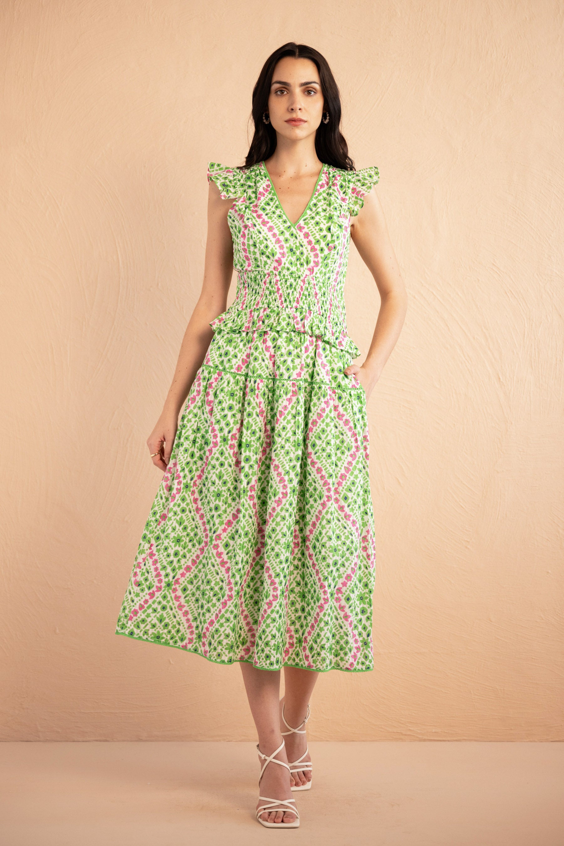 Front view of the Keira dress in a fresh green and pink Athena Heart print with floral and heart motifs. The dress features lace trim along the neckline and sleeves, a smocked waist for a flattering fit, and soft frill accents. The A-line skirt falls to the shin, and the dress includes discreet side pockets.