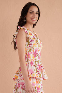 Side view of a woman wearing a sleeveless, floral printed top with ruffle sleeves, smocked waist, and peplum hem in shades of pink, orange, and green. Side view of a woman wearing a sleeveless, floral printed top with ruffle sleeves, smocked waist, and peplum hem in shades of pink, orange, and green.
