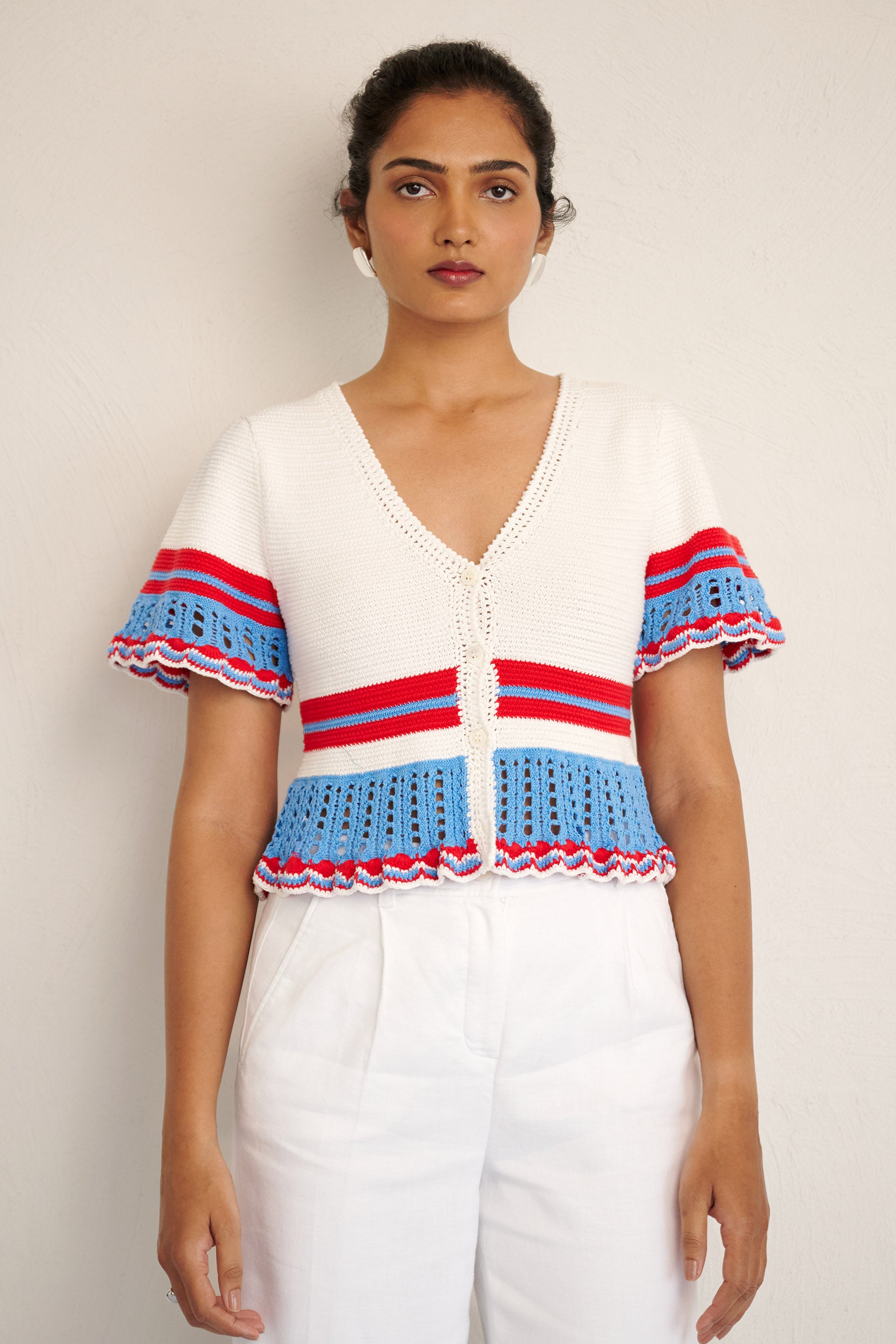 Front view of woman standing. She is wearing the Laura short-sleeve cardigan in white cotton, featuring hand-crocheted trims, a button-front placket, and a cropped, structured silhouette.
