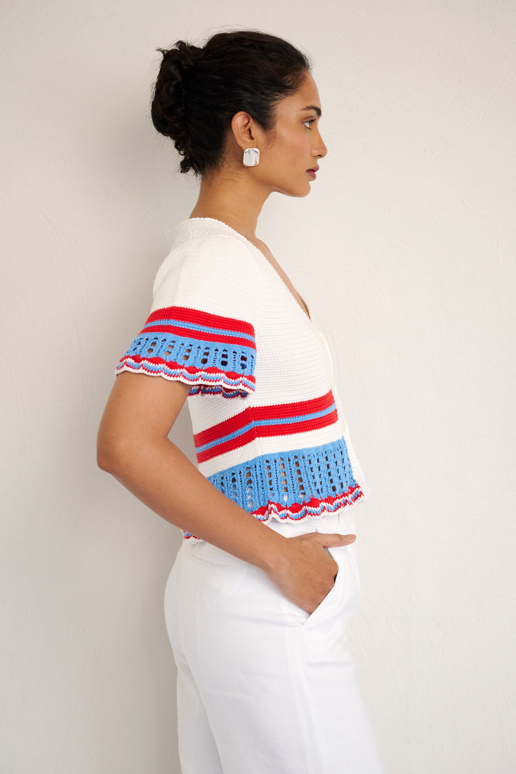 Side view of woman standing. She is wearing the Laura short-sleeve cardigan in white cotton, featuring hand-crocheted trims, a button-front placket, and a cropped, structured silhouette.
