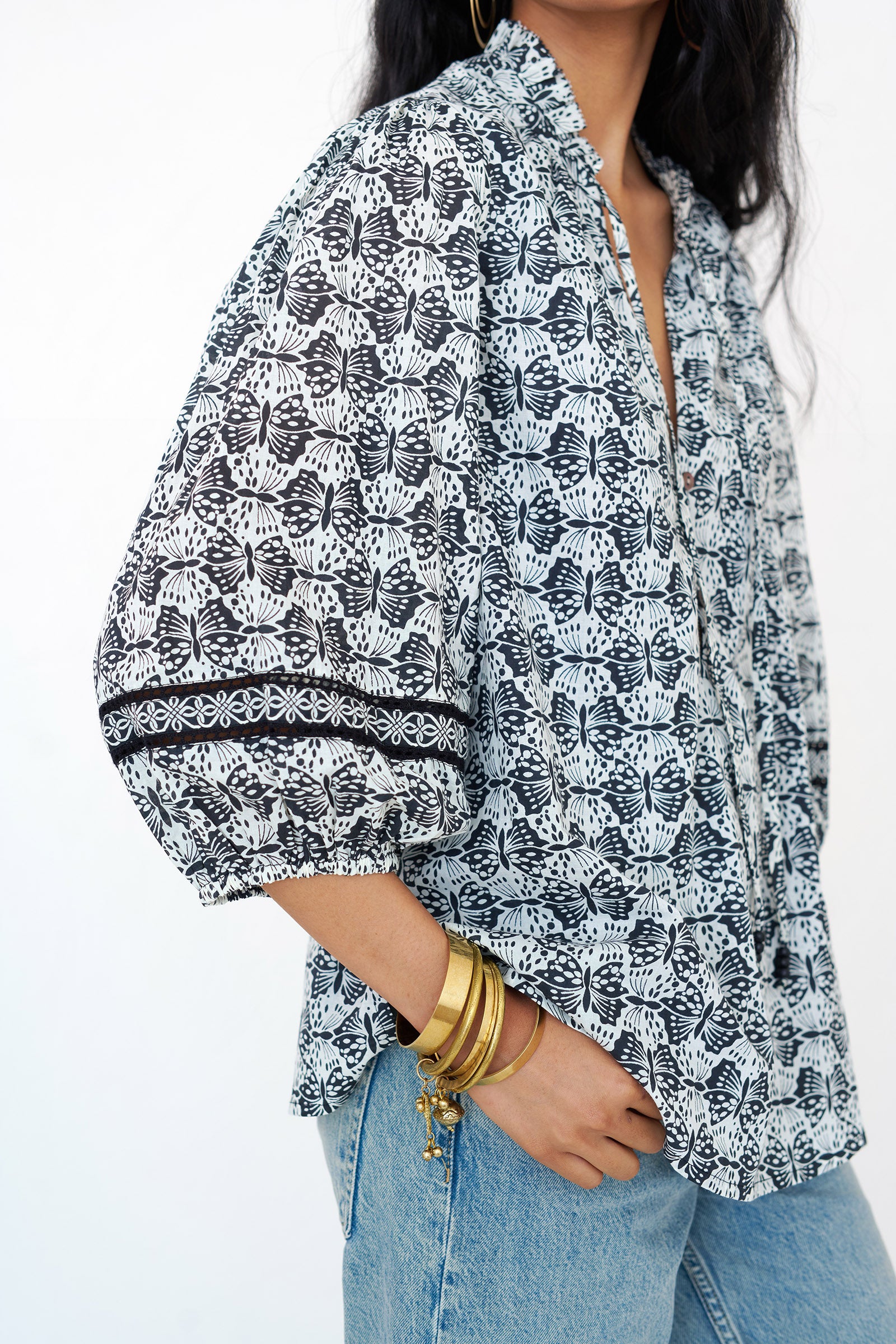 Side view close up of a woman standing wearing the Lorna top in Flutter print, featuring Celtic-knot lace sleeve inserts, and a loose cotton voile silhouette styled with jeans