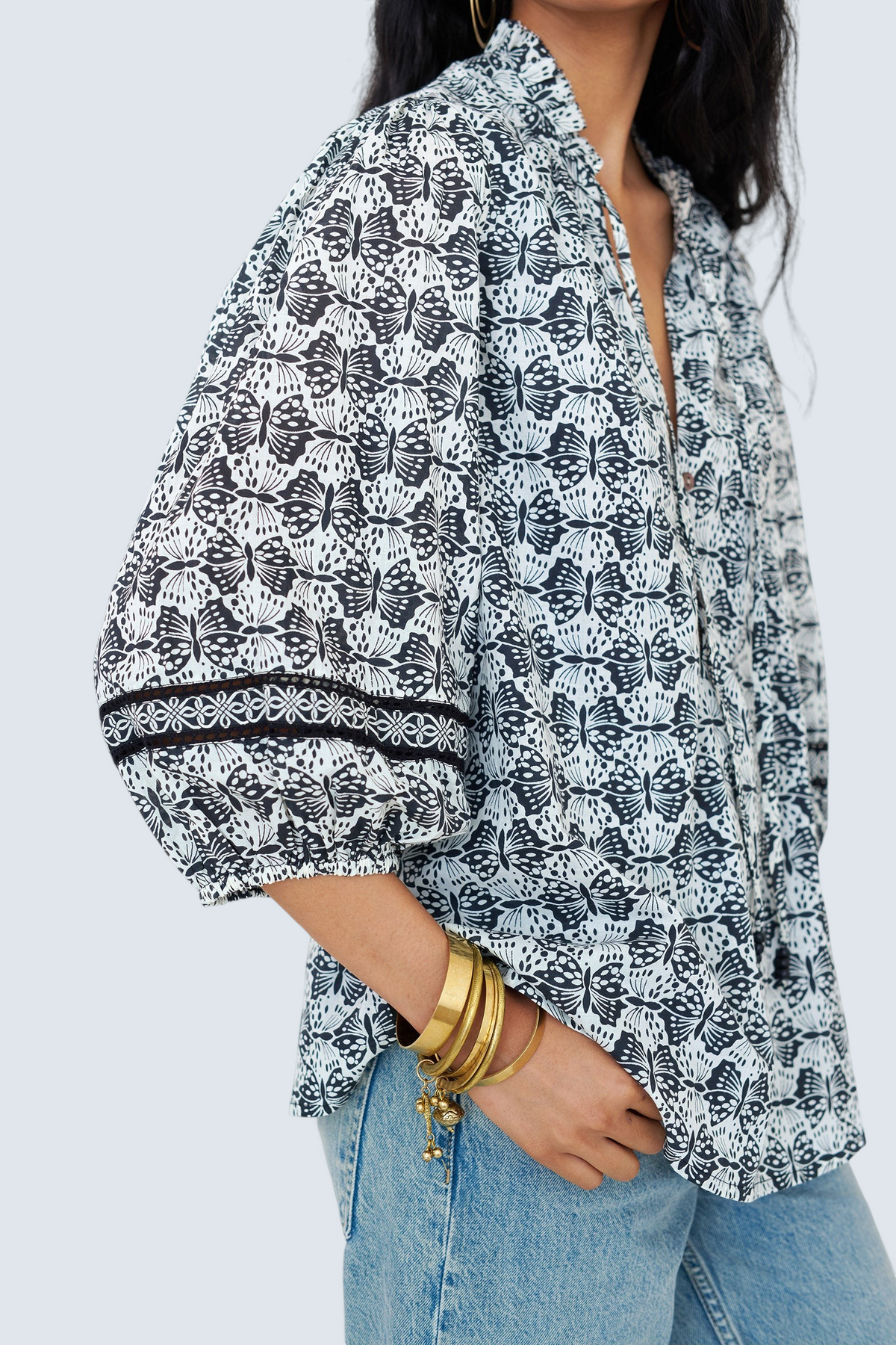 Side view close up of a woman standing wearing the Lorna top in Flutter print, featuring Celtic-knot lace sleeve inserts, and a loose cotton voile silhouette styled with jeans