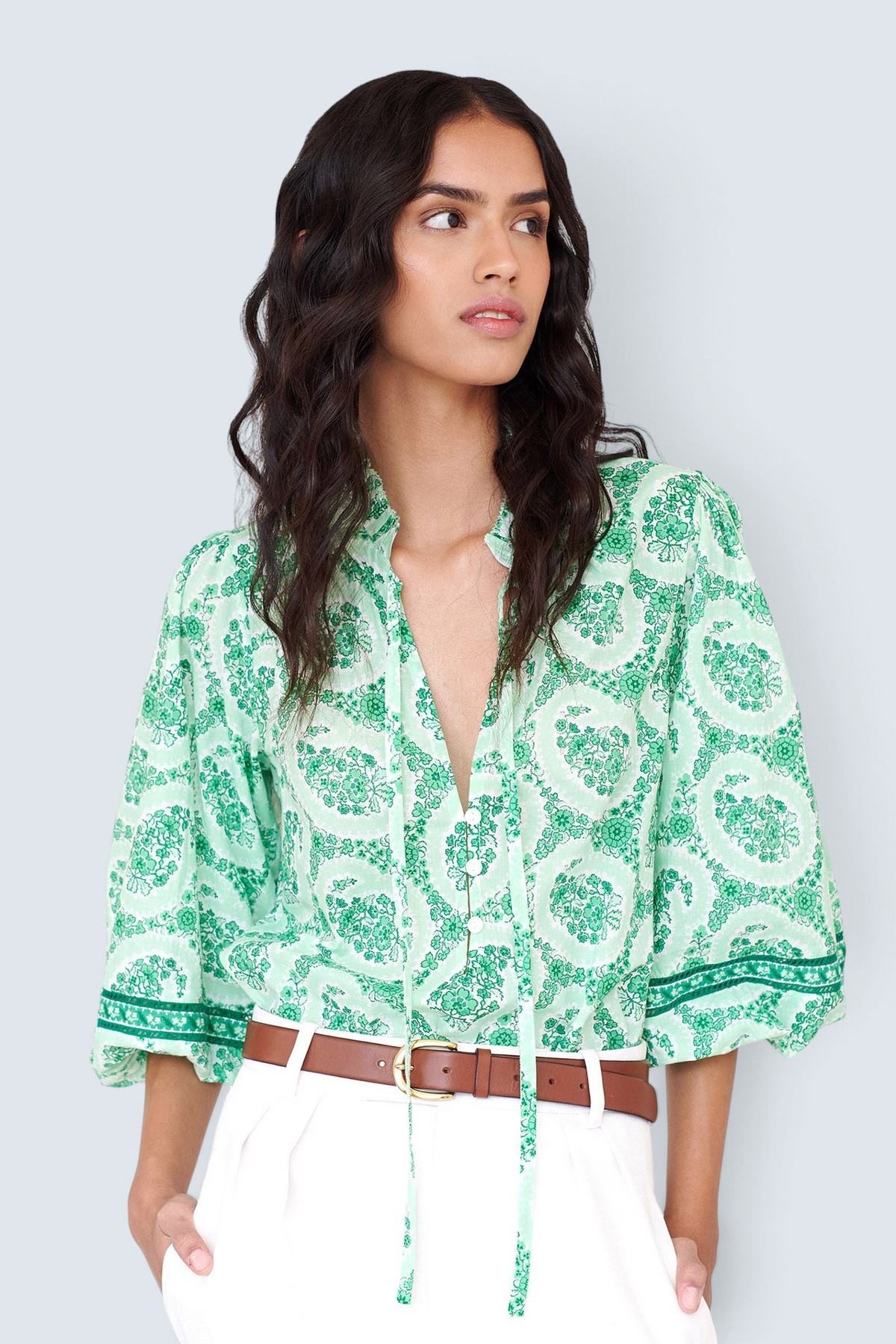 Front view closeup of a woman standing. She is wearing the Lorna top in Paisley Copse print, featuring a ruffled V-neck with tie & contrast sleeve trim.