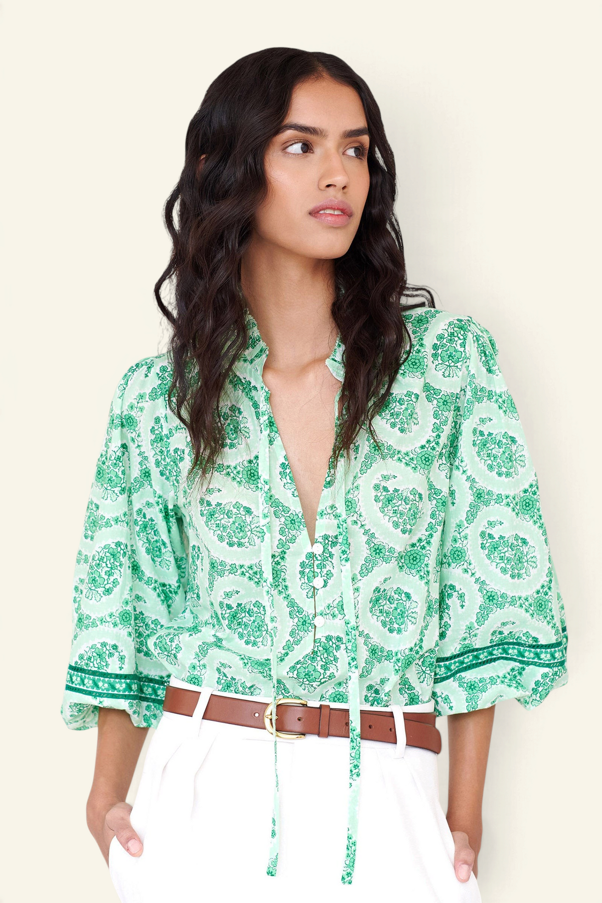 Front view closeup of a woman standing. She is wearing the Lorna top in Paisley Copse print, featuring a ruffled V-neck with tie & contrast sleeve trim.