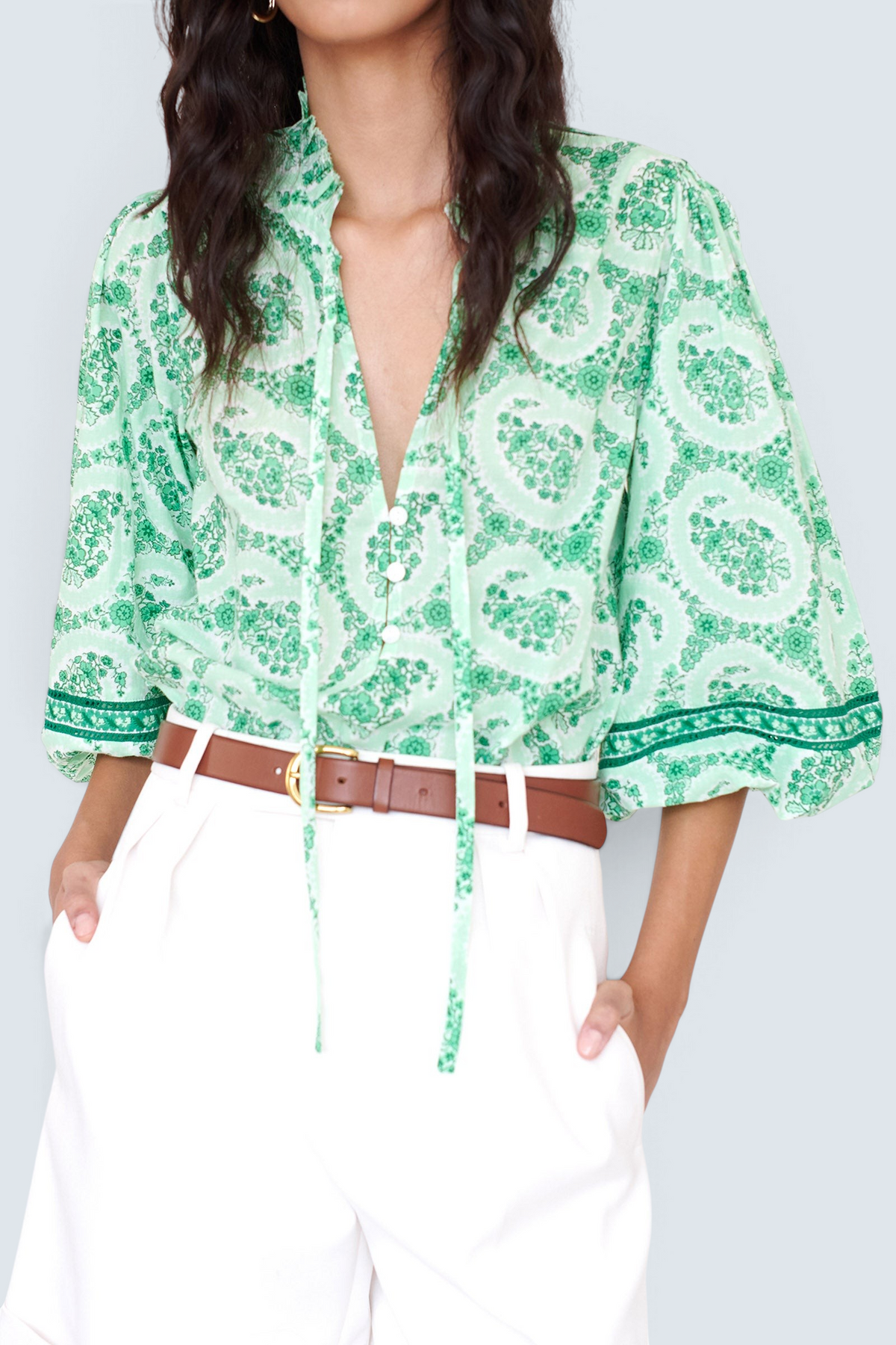 Front view closeup of a woman standing. She is wearing the Lorna top in Paisley Copse print, featuring a ruffled V-neck with tie & contrast sleeve trim.