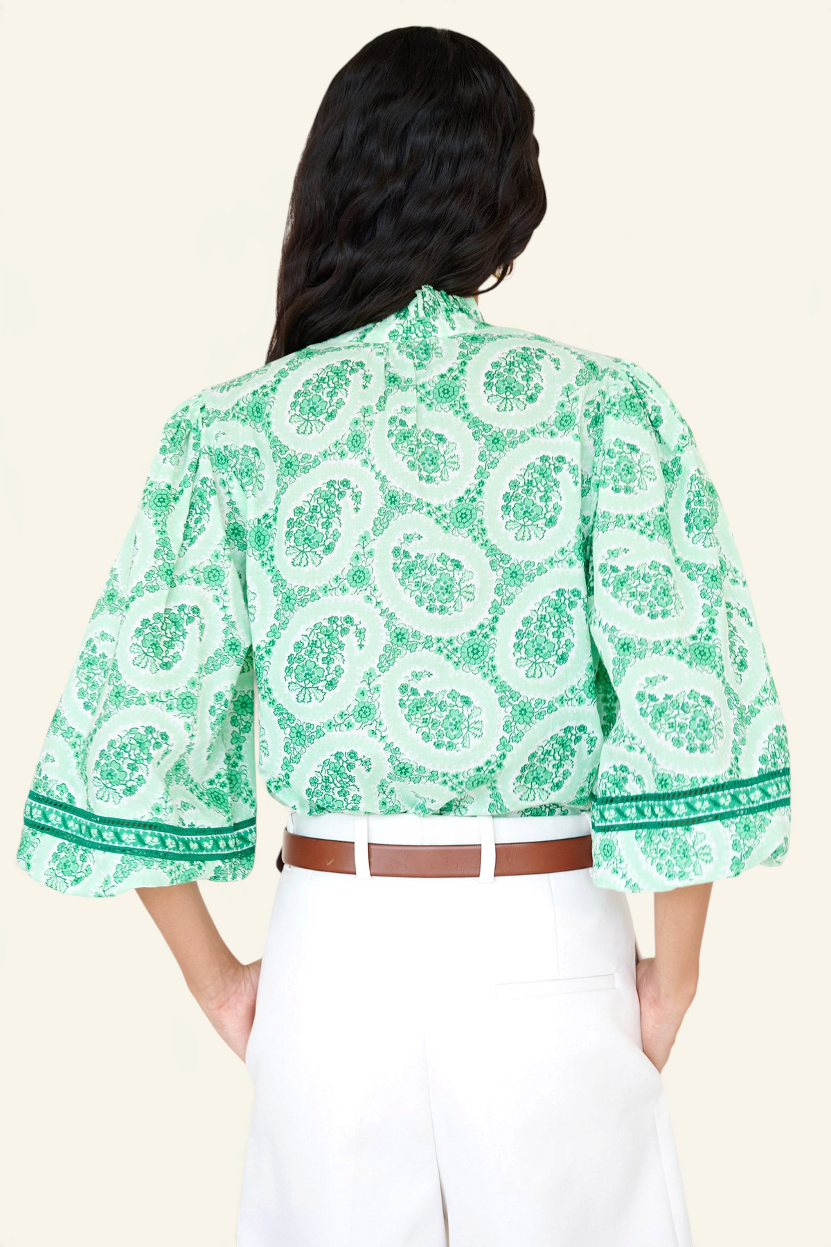 Back view closeup of a woman standing. She is wearing the Lorna top in Paisley Copse print, featuring a ruffled V-neck with tie & contrast sleeve trim.