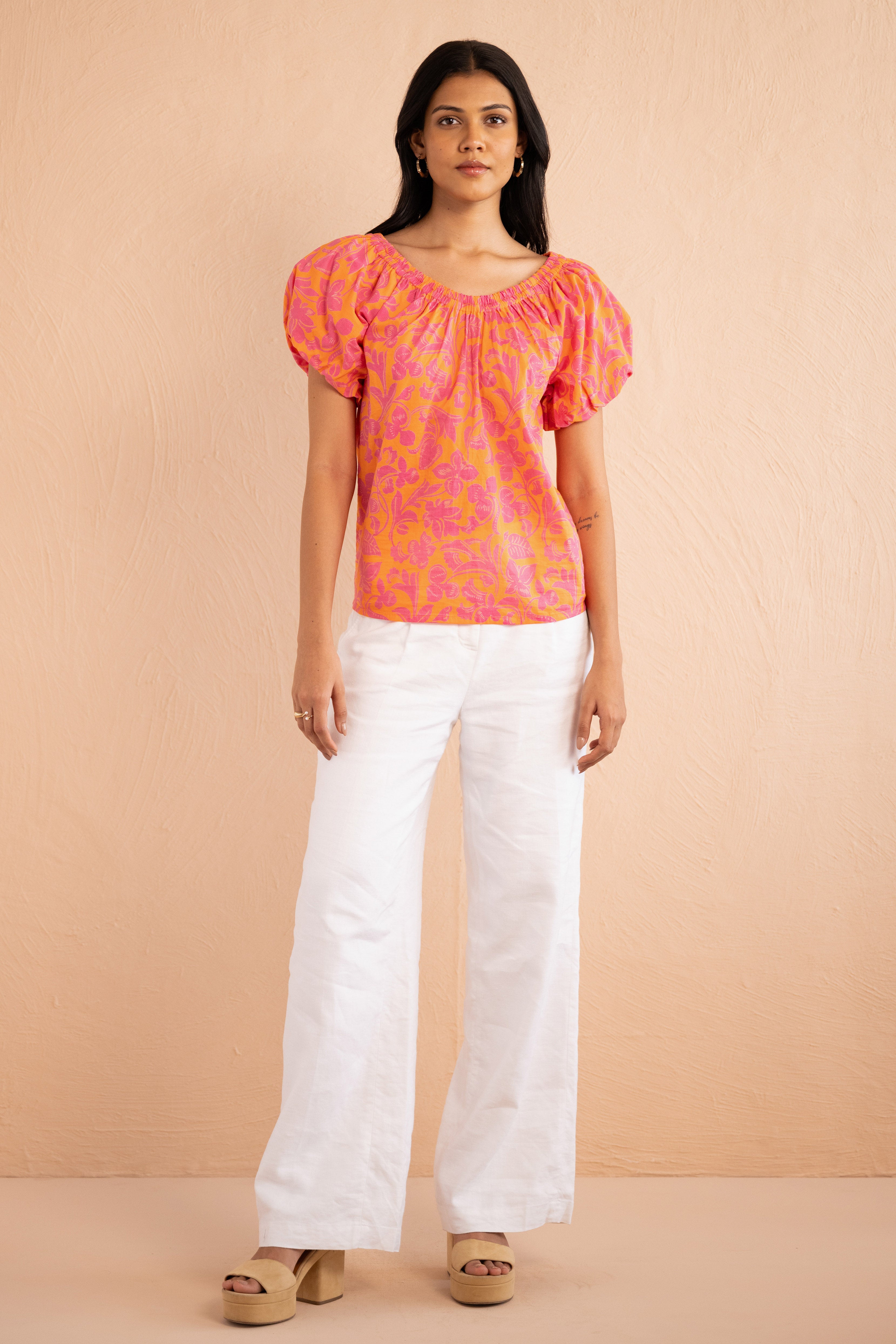 Front view of model wearing Louise Top in Gaia Nectarine print paired with white pants. Front view of model wearing Louise Top in Gaia Nectarine print paired with white pants.