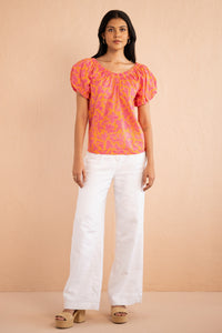 Front view of model wearing Louise Top in Gaia Nectarine print paired with white pants. Front view of model wearing Louise Top in Gaia Nectarine print paired with white pants.