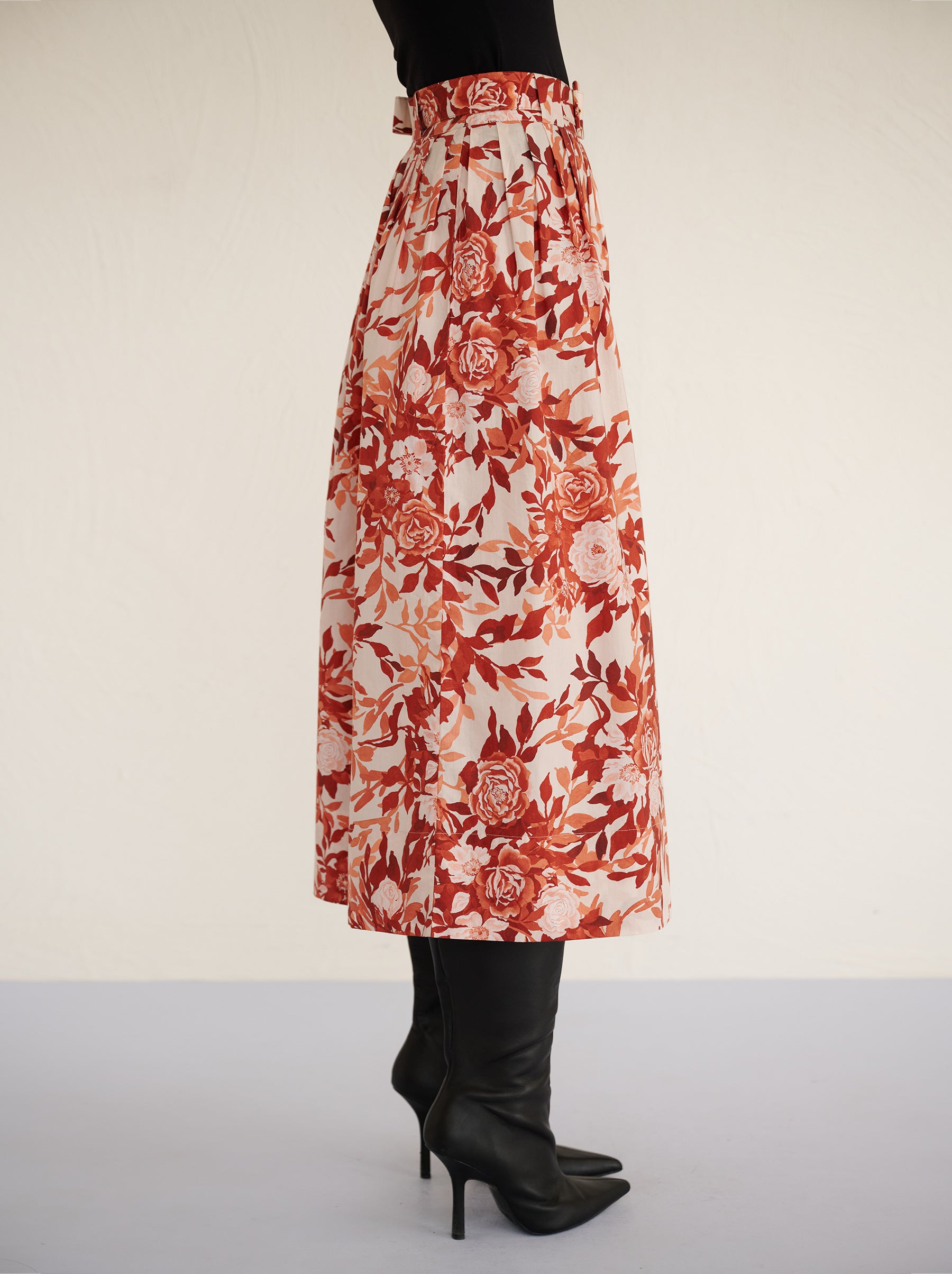 Side view close up of a model standing. She is wearing the Magdalena skirt in the Bibi Rose print. It is featuring soft all-around pleats, side-seam pockets, and a back zipper fastening for a classic, flattering silhouette.