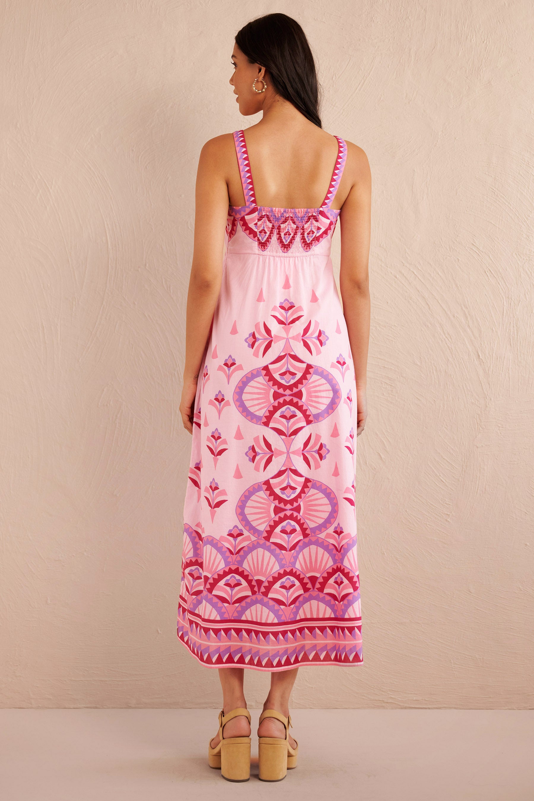 Back view of woman wearing a sleeveless pink midi dress with bold geometric amethyst and fuchsia prints, styled with platform sandals.