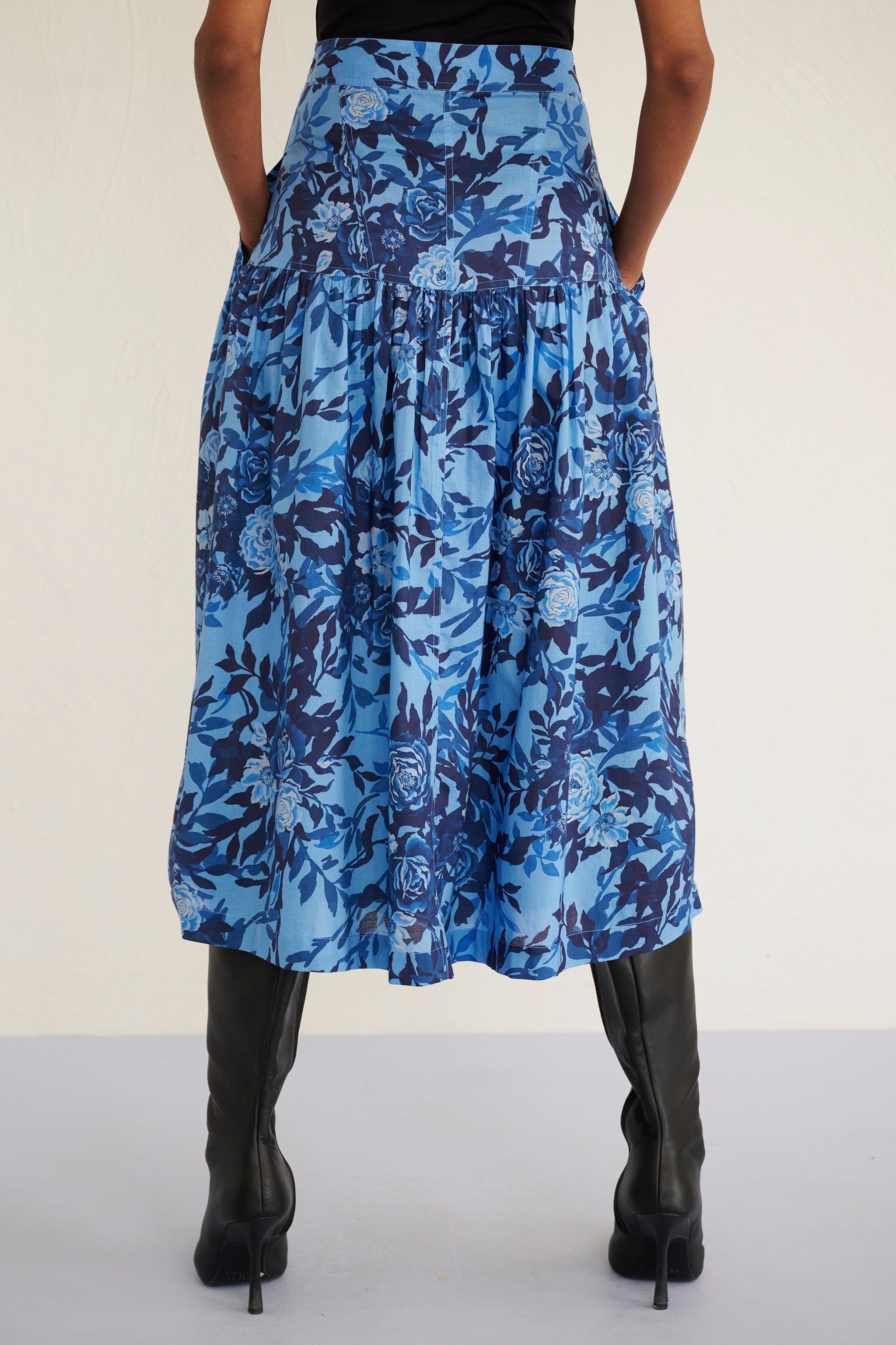 Back view of woman wearing a high-waisted floral midi skirt with a gathered silhouette and side pockets, featuring a soft watercolor rose print.