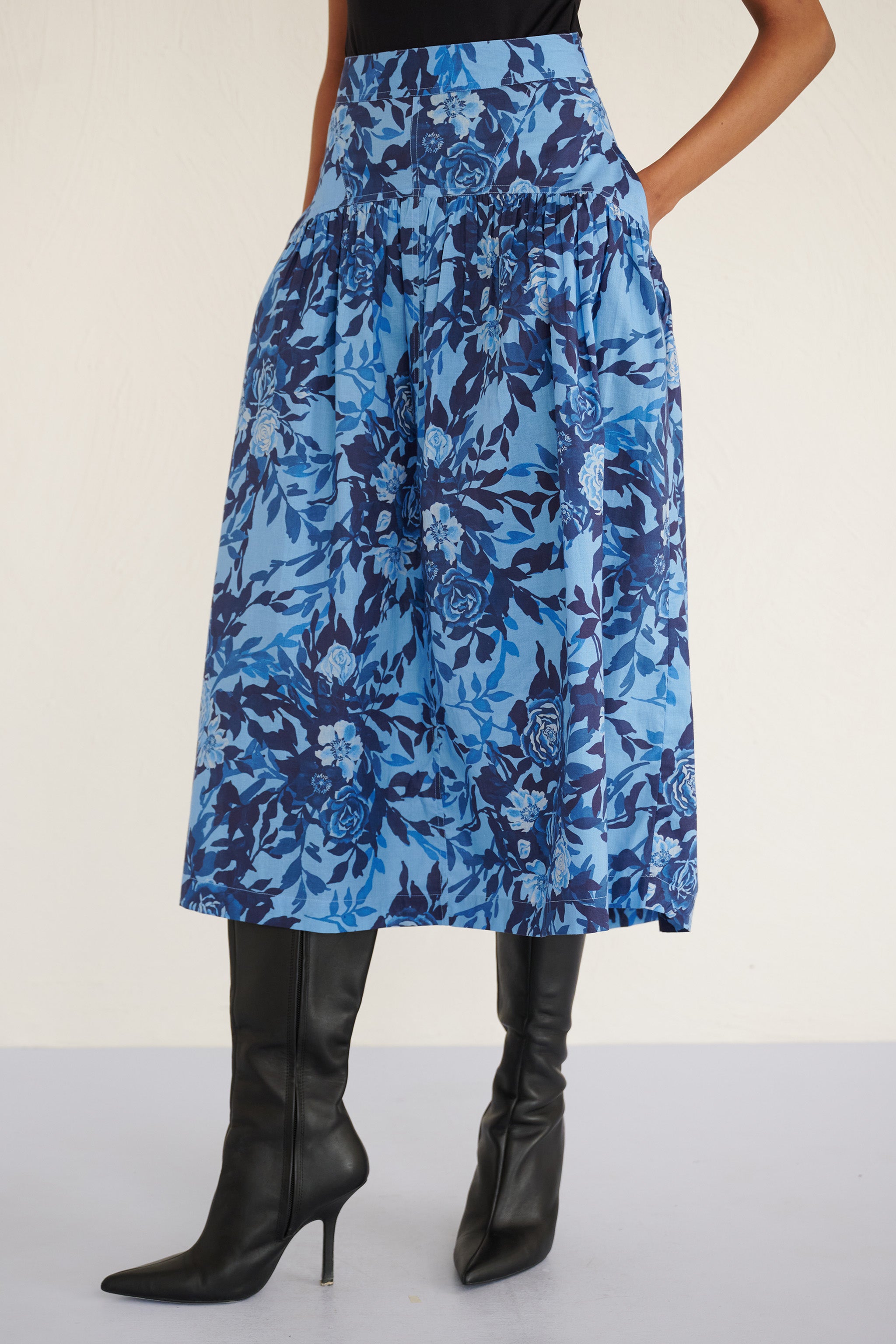 Side view of woman wearing a high-waisted floral midi skirt with a gathered silhouette and side pockets, featuring a soft watercolor rose print.