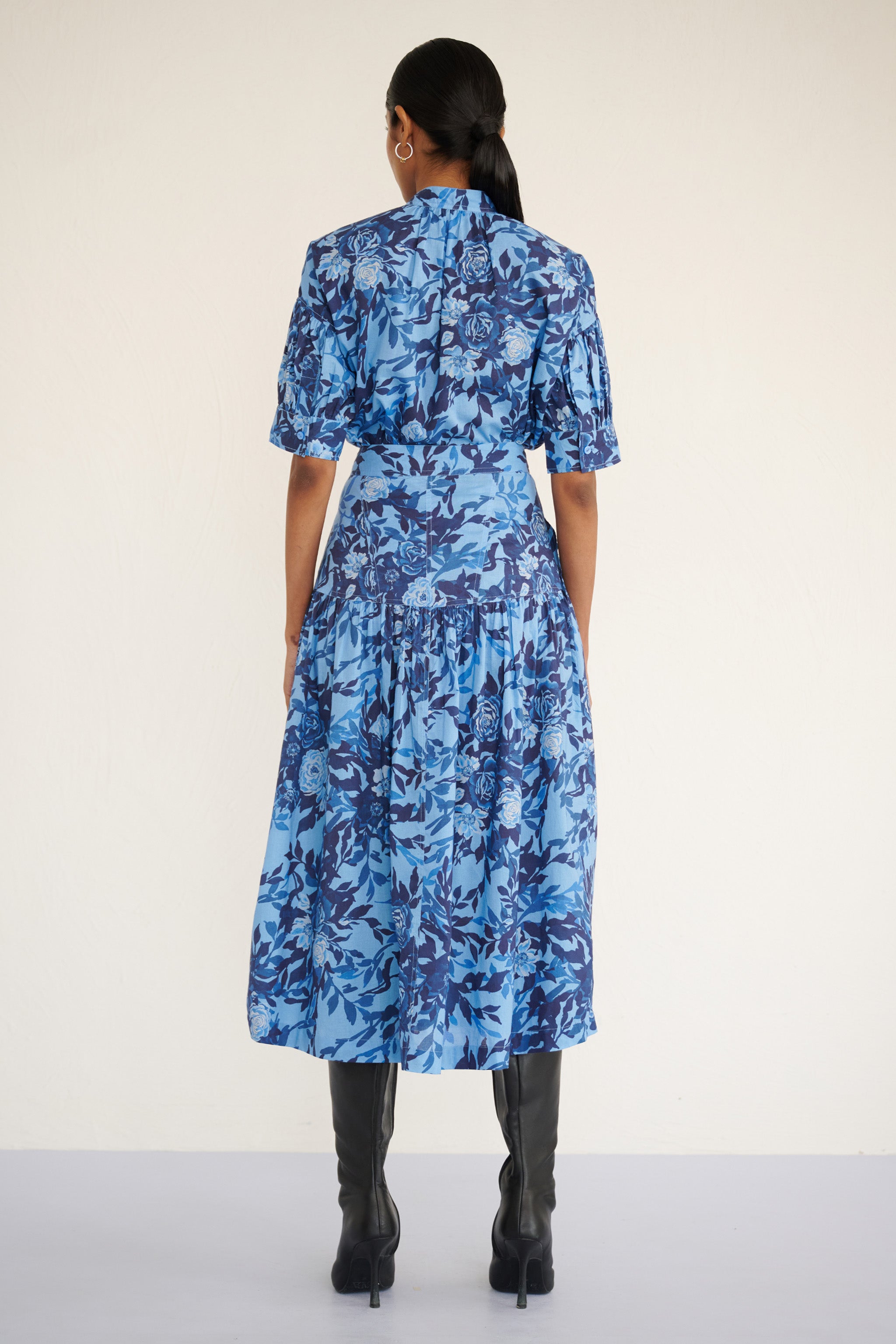 Back view of woman wearing a high-waisted floral midi skirt with a gathered silhouette and side pockets, featuring a soft watercolor rose print paired with Ivy shirt in same print.