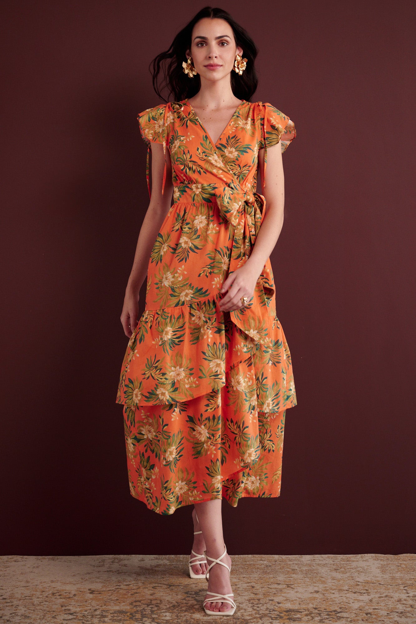 Side view of woman walking. She is wearing the Mercy wrap dress in Artichoke Flower print. It has asymmetrical tiers, adjustable shoulder drawstrings, breezy cotton voile fabric, and side-seam pockets, inspired by 15th-century embroidered tapestry motifs.