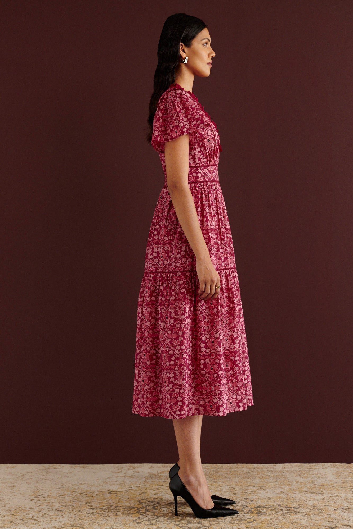 Side view of woman standing. She is wearing the Naxos midi dress in Ottoman print, with plunging V-neck trimmed in red lace, lace insets at waist and skirt, flutter sleeves, smooth cotton cambric, fully lined construction, and side-seam pockets.