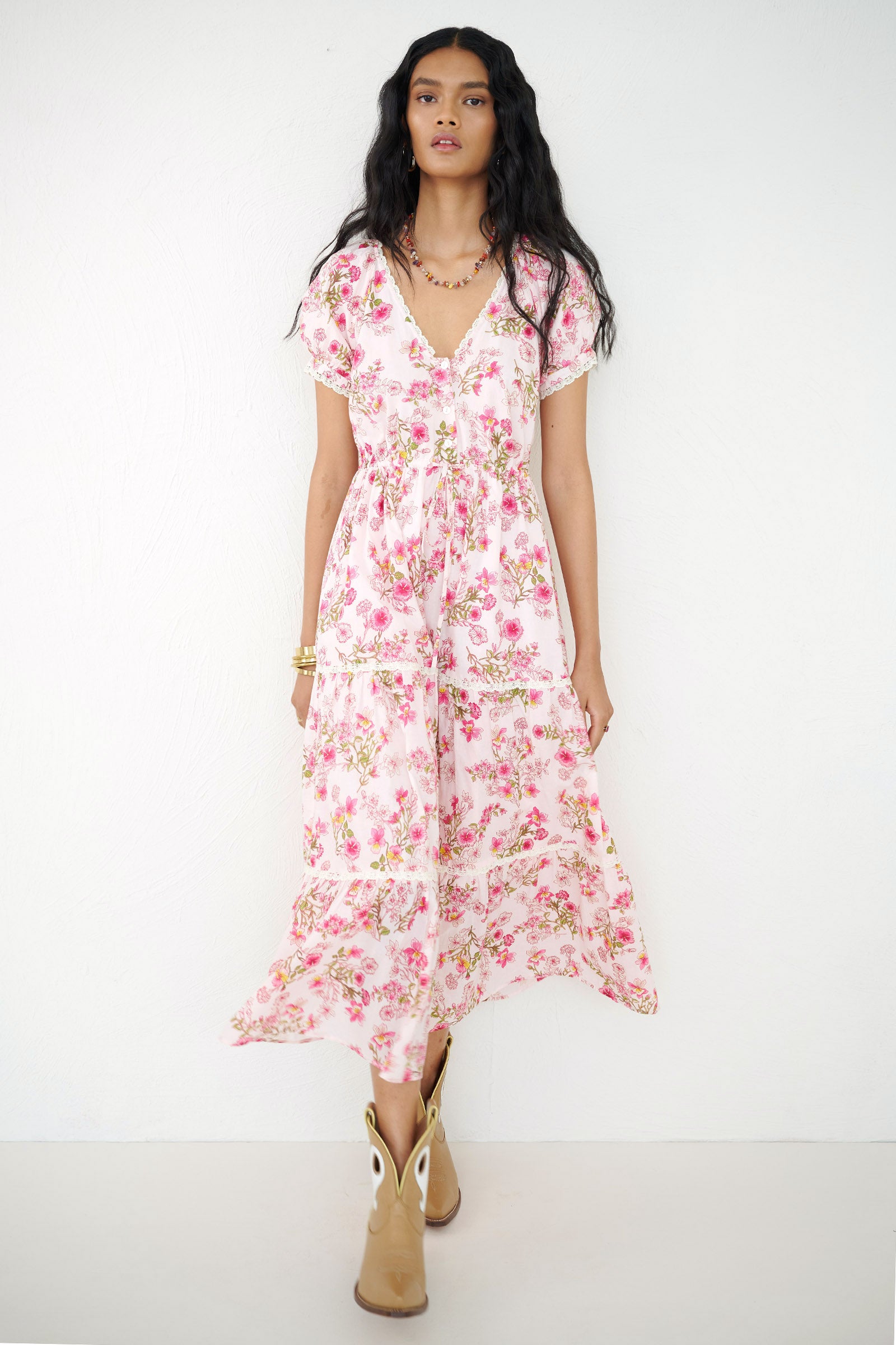 Front view of a woman standing wearing the Poppy dress in Burdock floral print, featuring raglan blouson sleeves, front button placket, drawstring waist, lace-trimmed tiers, flowing skirt, and side-seam pockets.