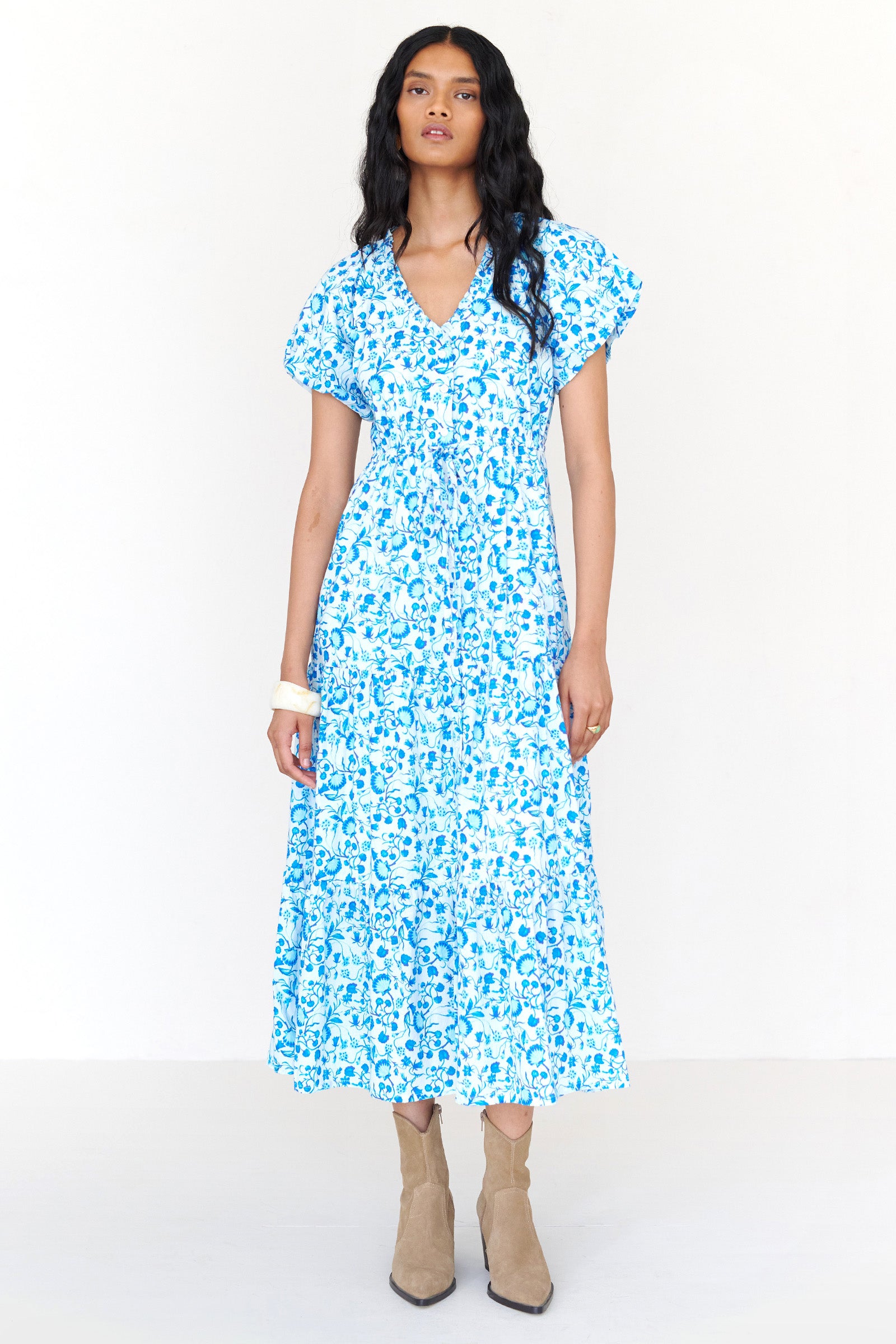 Front view of a woman standing wearing the Poppy dress in Clam Garland print. It features raglan blouson sleeves, front button placket, drawstring waist, flowing skirt and side-seam pockets.