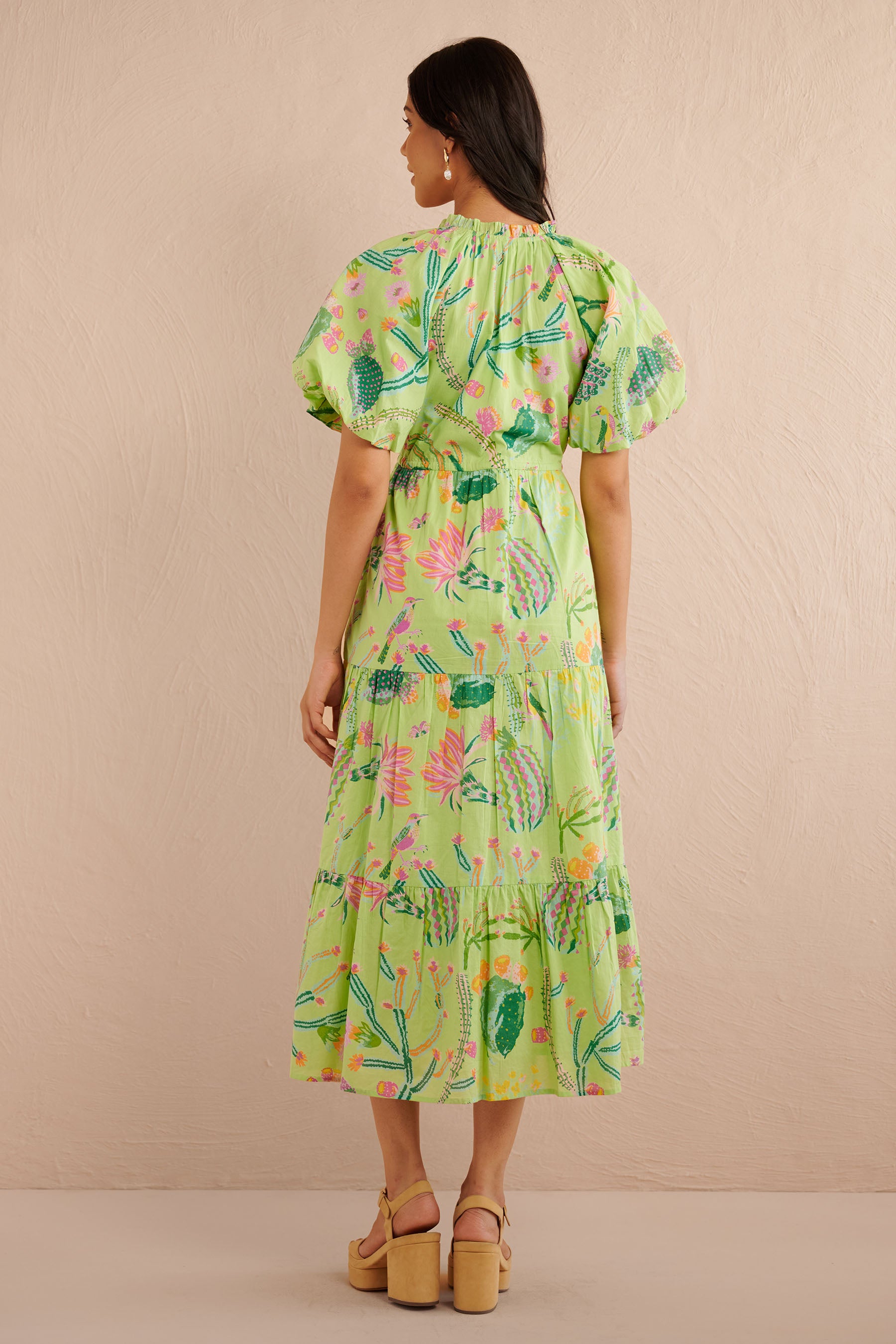 Back view of the Poppy dress in a green Calypso Cacti print with blouson sleeves, button front, drawstring waist, and a flowing tiered skirt featuring desert blooms, birds, and butterflies.