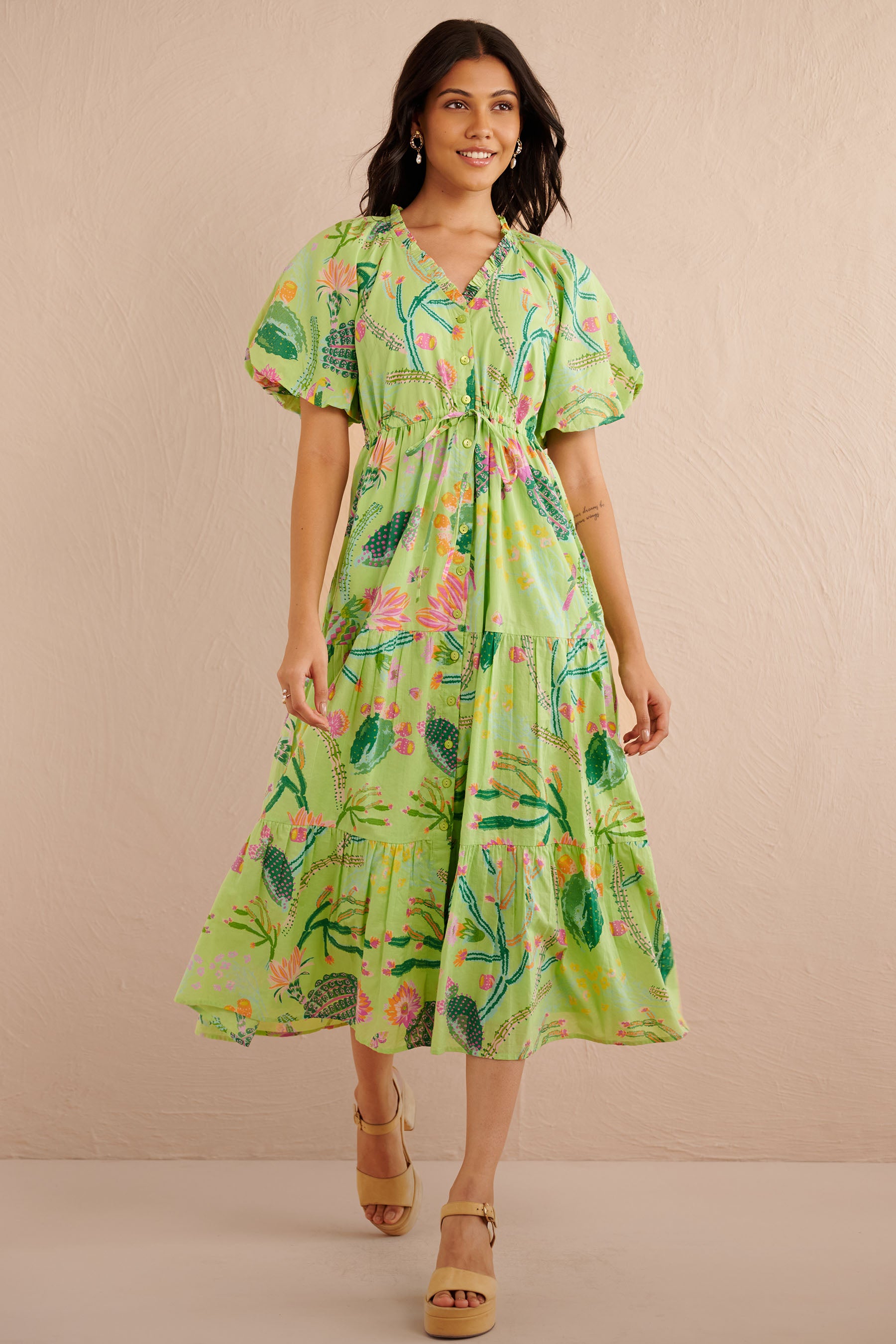 Front view of the Poppy dress in a green Calypso Cacti print with blouson sleeves, button front, drawstring waist, and a flowing tiered skirt featuring desert blooms, birds, and butterflies.