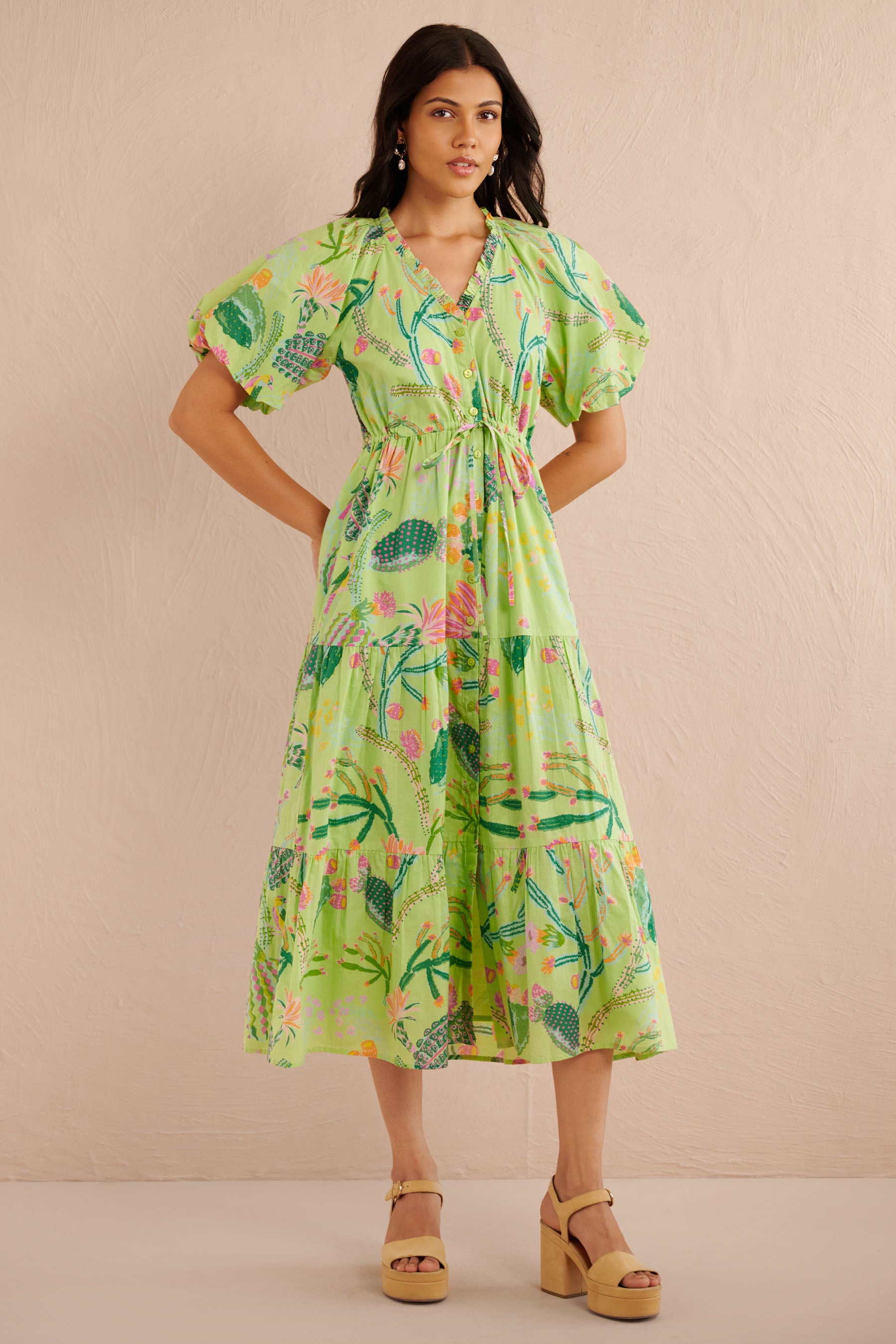 Front view of the Poppy dress in a green Calypso Cacti print with blouson sleeves, button front, drawstring waist, and a flowing tiered skirt featuring desert blooms, birds, and butterflies.