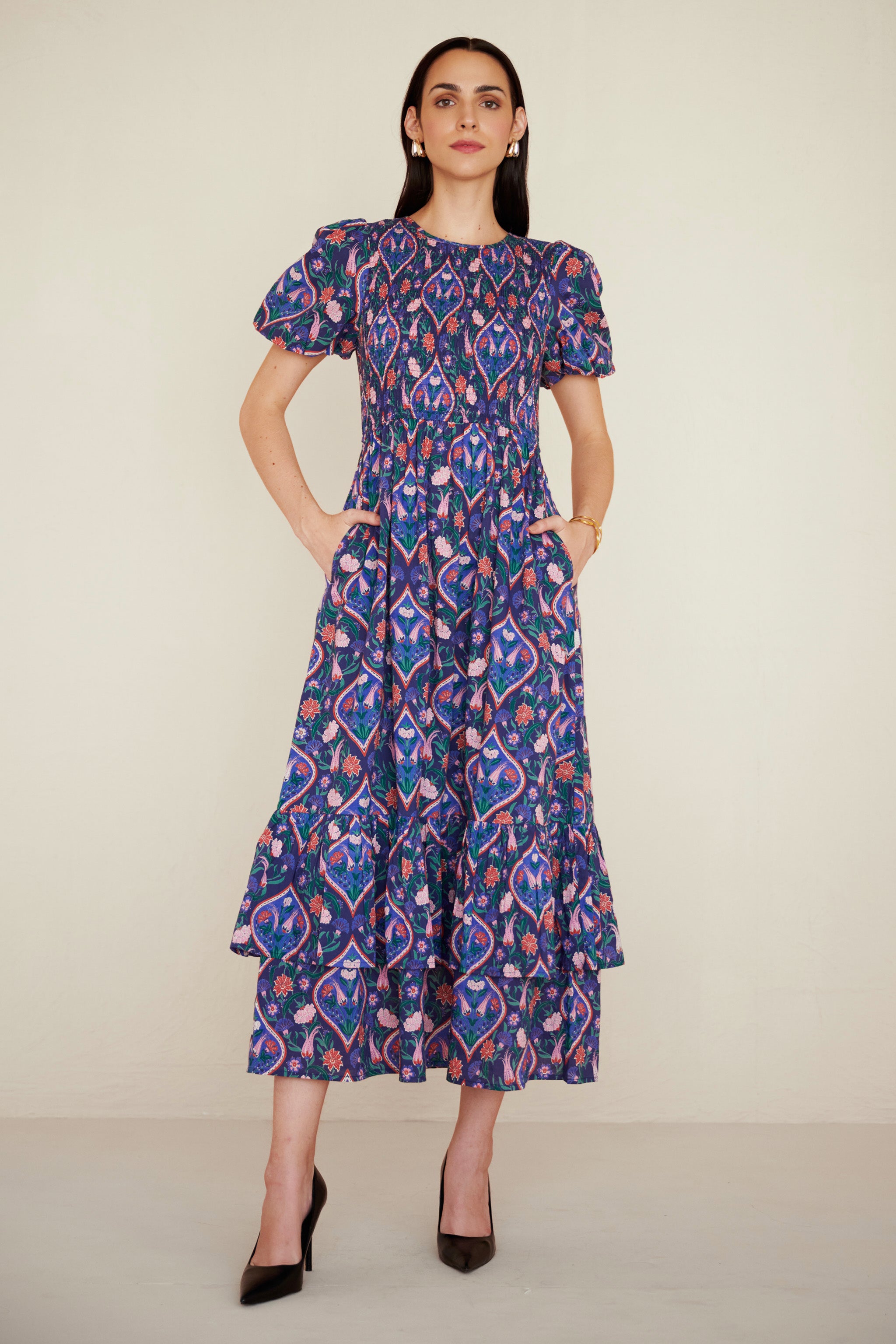 Front view of woman wearing a midi dress with smocked bodice, puff sleeves, and tiered skirt, featuring a floral tile print inspired by Uzbek design.