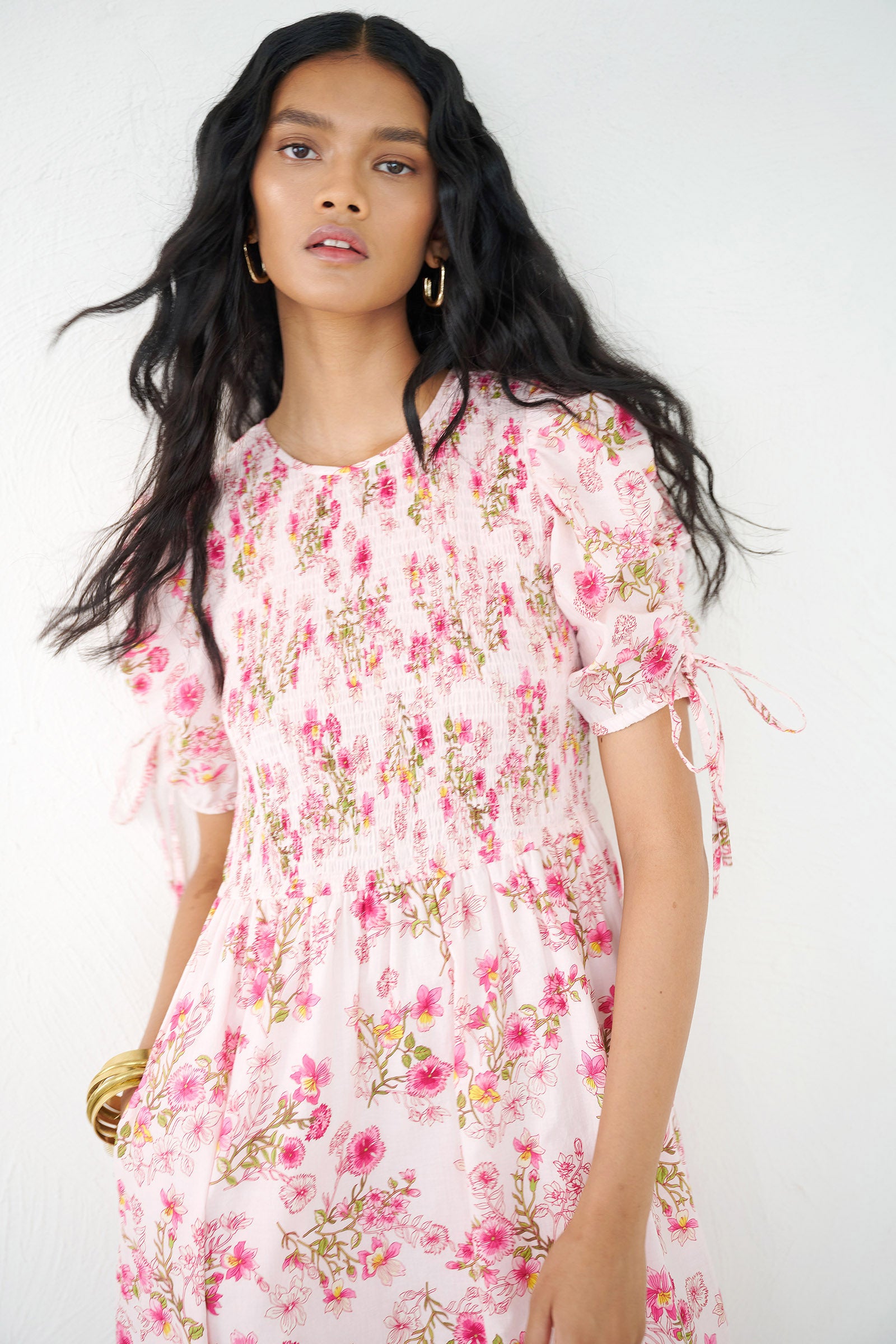 Front view close up of a woman standing wearing the Queenie midi dress in Burdock floral print, featuring a smocked bodice, drawstring sleeves, full skirt & pockets.