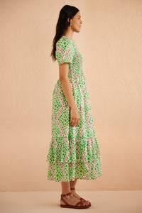 Side view of woman wearing the Quant midi dress in Athena Heart print, featuring a smocked bodice, puffed sleeves, tiered full skirt, lace trim, and side pockets in a green and pink floral-heart motif. Side view of woman wearing the Quant midi dress in Athena Heart print, featuring a smocked bodice, puffed sleeves, tiered full skirt, lace trim, and side pockets in a green and pink floral-heart motif.