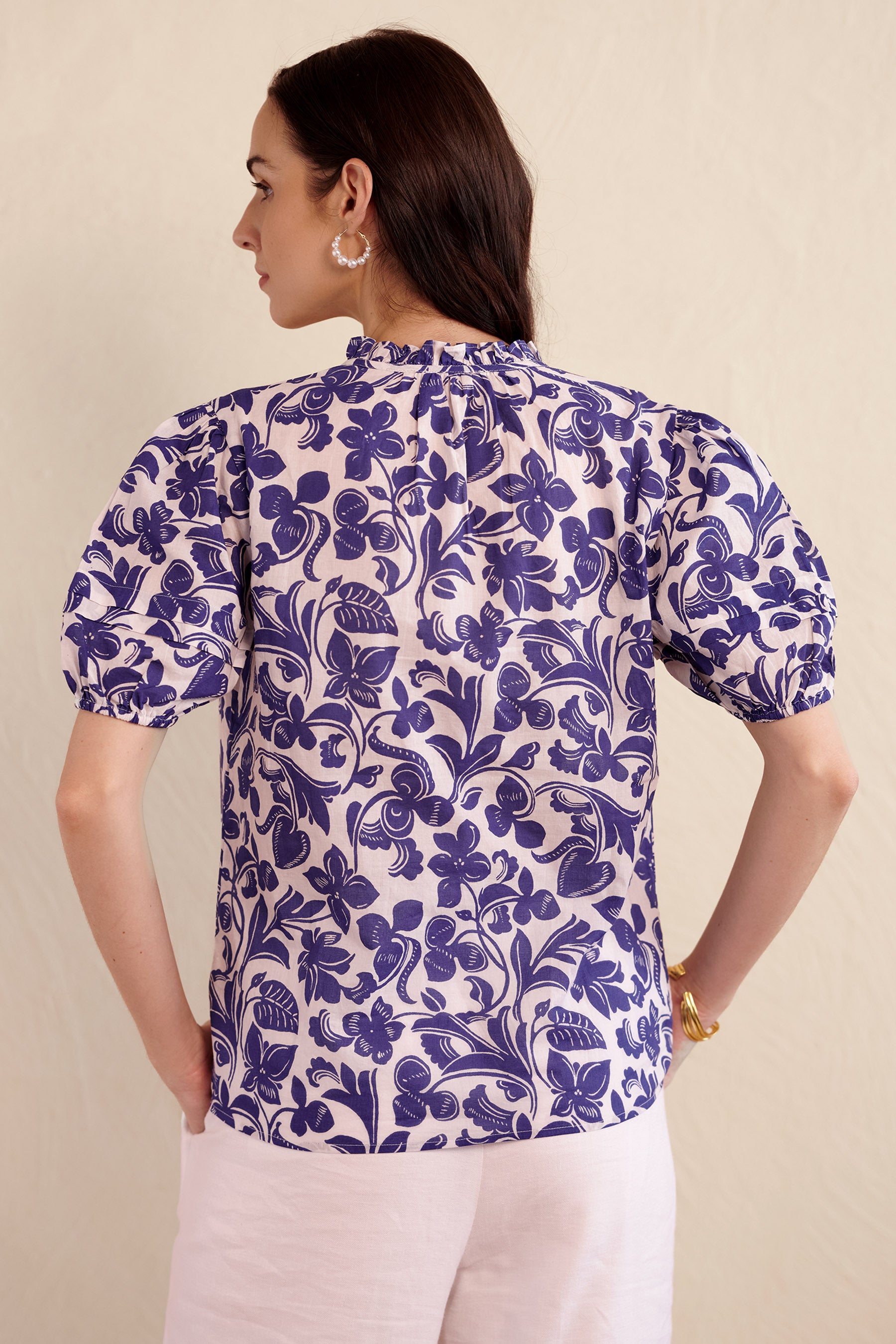 Back view of woman wearing the Bronte top in blue and white Gaia floral print, featuring a front opening, pleated sleeves, and delicate neckline detailing.