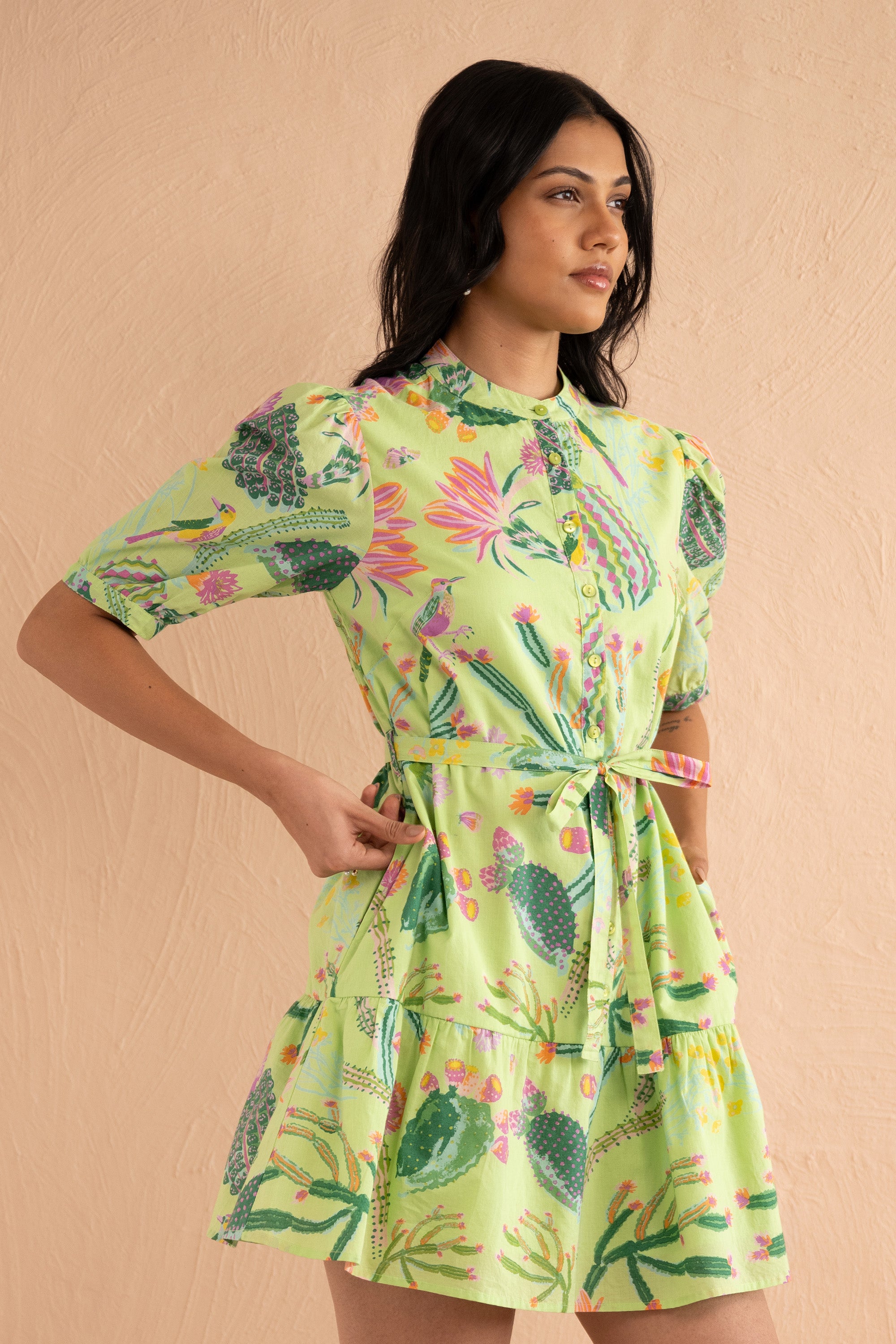 Front view close up of woman wearing Roma mini shirtdress in hand-screen-printed Calypso Cacti pattern, featuring blooming succulents, desert blossoms, birds, butterflies, detachable belt, and side-seam pockets in lightweight cotton voile.