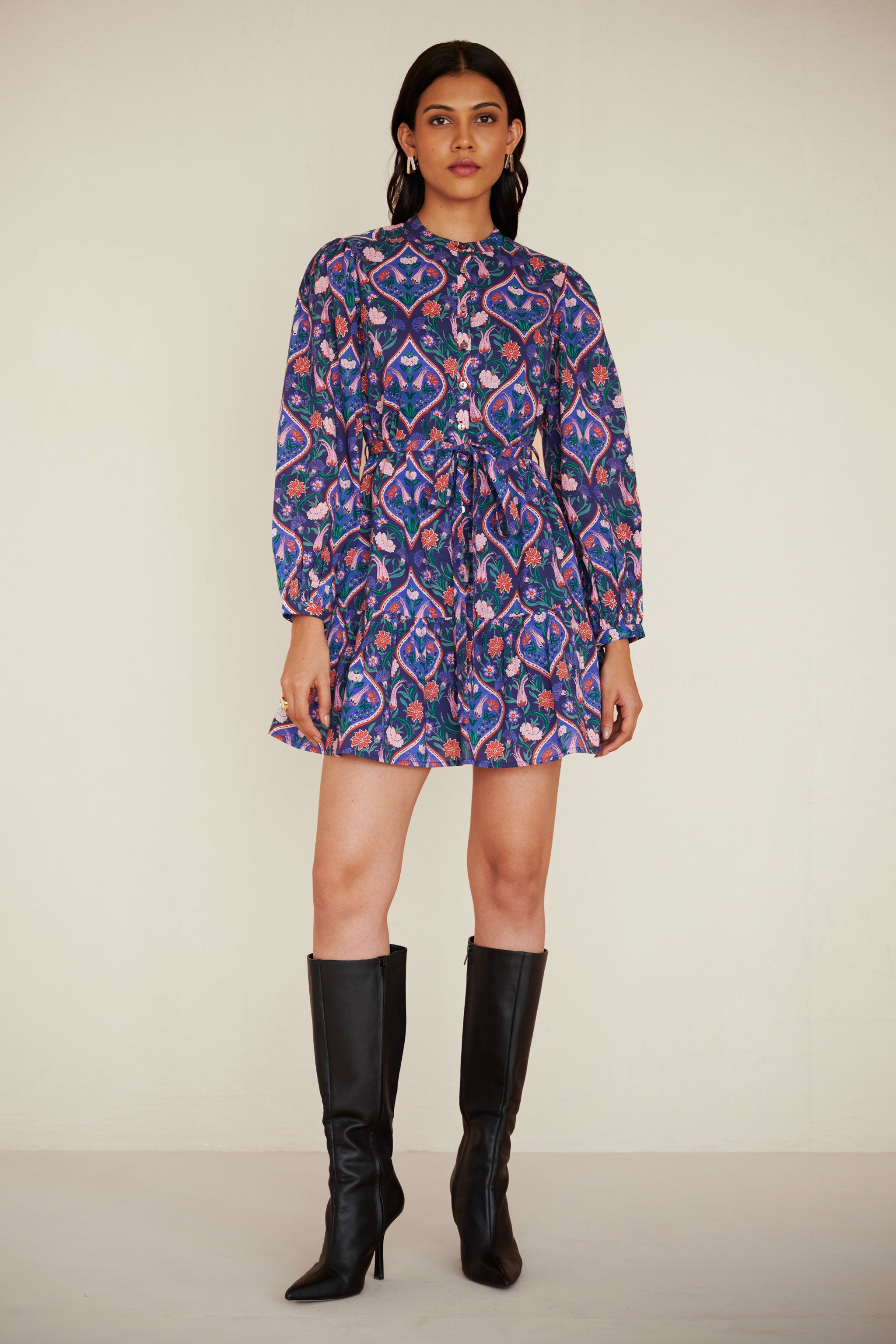 Front view of woman wearing a cotton mini dress with wrist-length sleeves, a floral tile print, and a detachable belt, styled with side pockets.