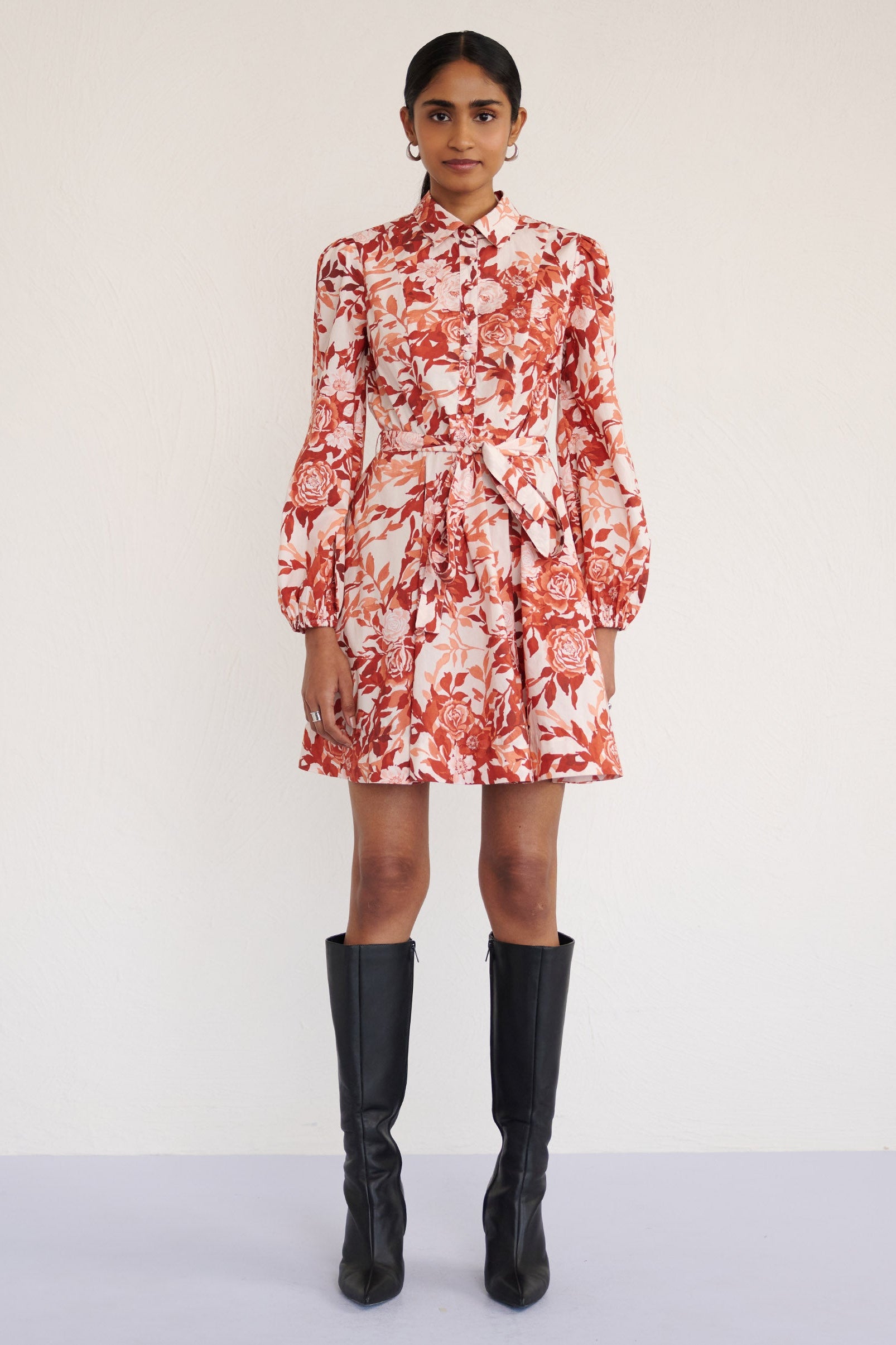 Front view of a model standing. She is wearing the Rowena mini shirtdress in crisp cotton poplin in Bibi Rose Chocolate print. It is featuring a delicate collar, lantern sleeves, short hem, full lining, and side-seam pockets.