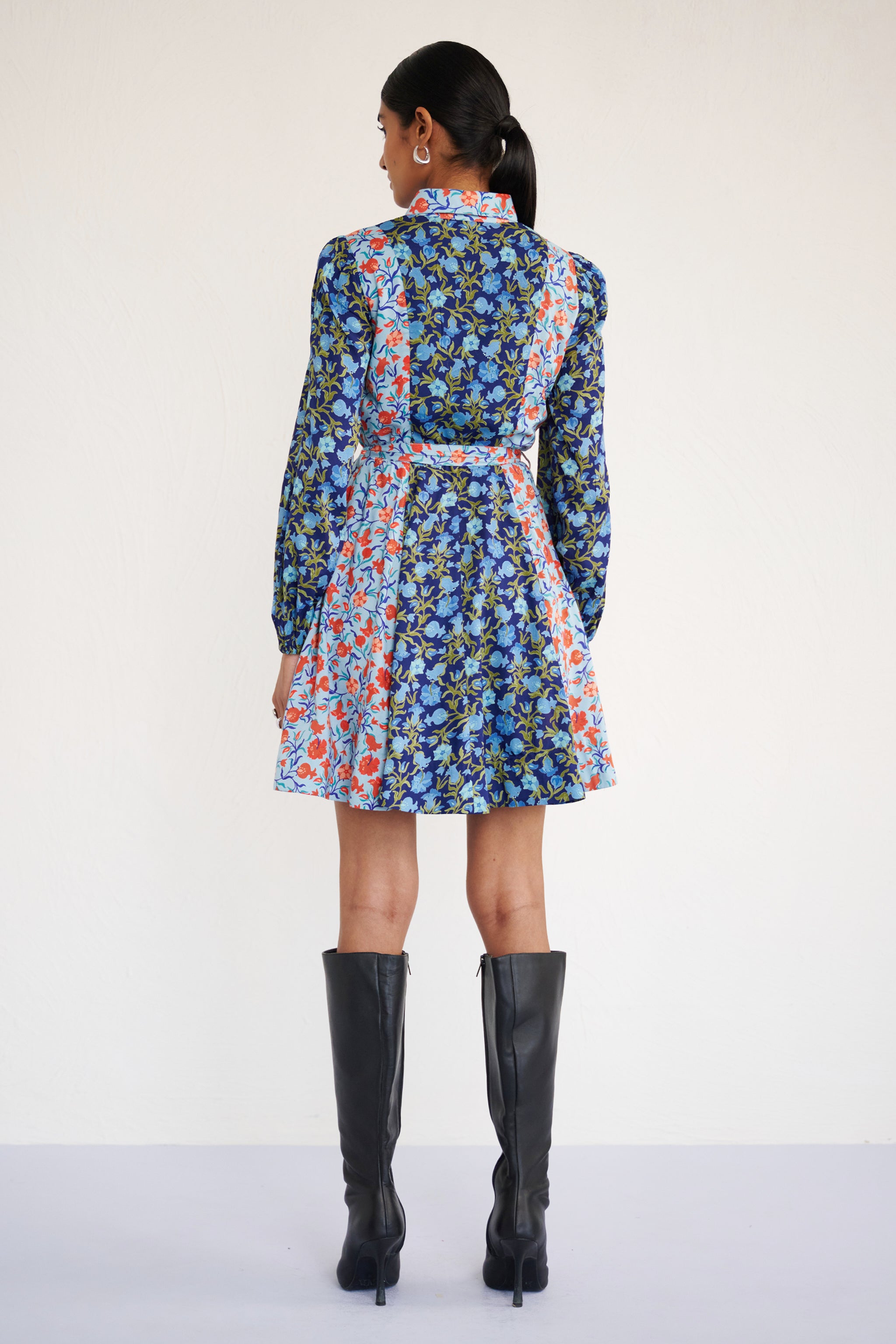 Back view of woman standing. She is wearing Rowena Dress in Pomegranate Vine print, Lapis color. It is a mini shirtdress with lantern sleeves, a delicate collar, and contrast pomegranate vine print, styled with side pockets.