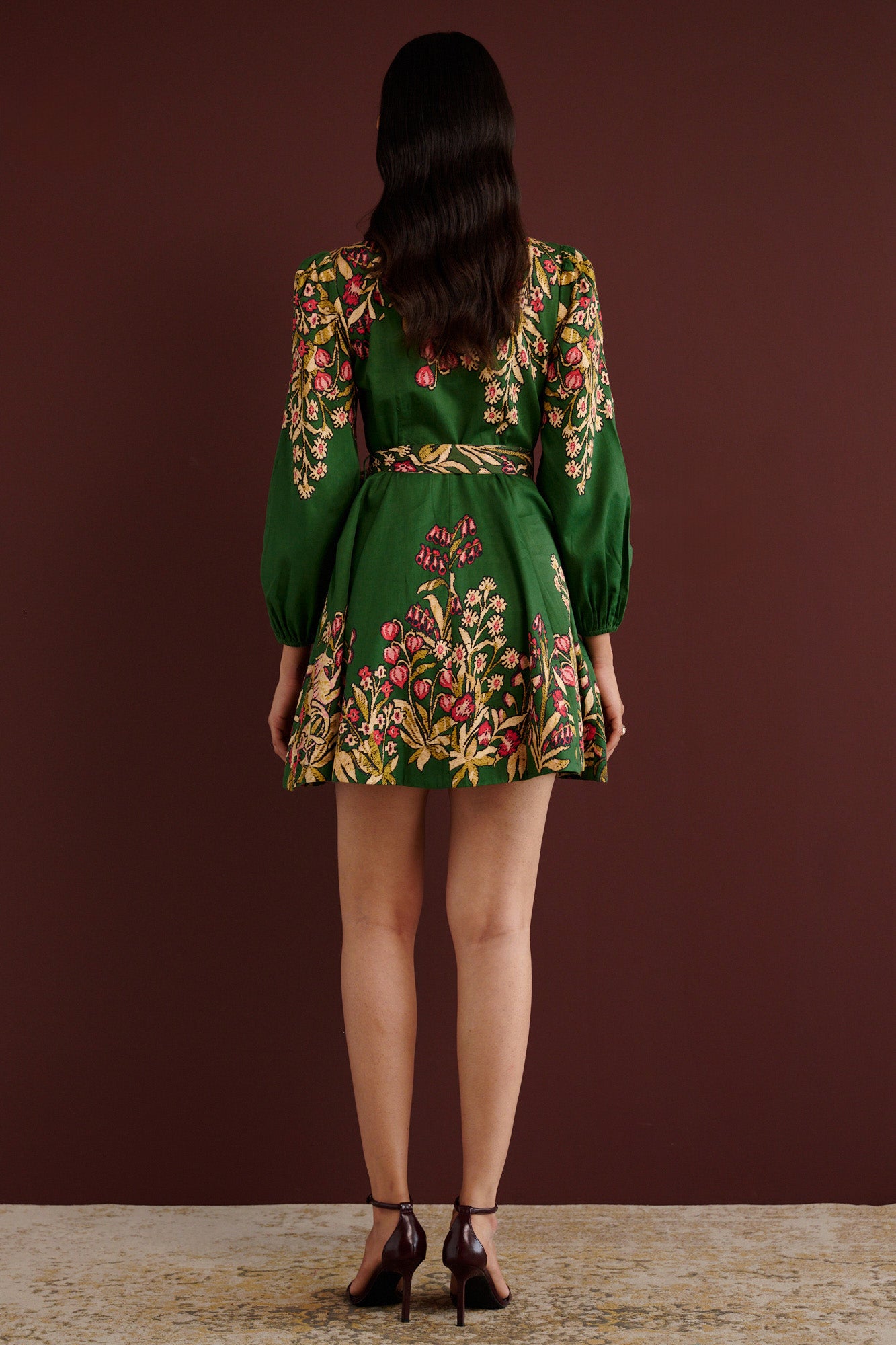 Back view of woman standing. She is wearing the Rowena mini shirtdress in Unicorn Tapestry print. It features a fitted bodice, delicate collar, lantern sleeves, short hem, side-seam pockets, and 15th-century-inspired enchanted garden motifs from the Scottish Highlands.
