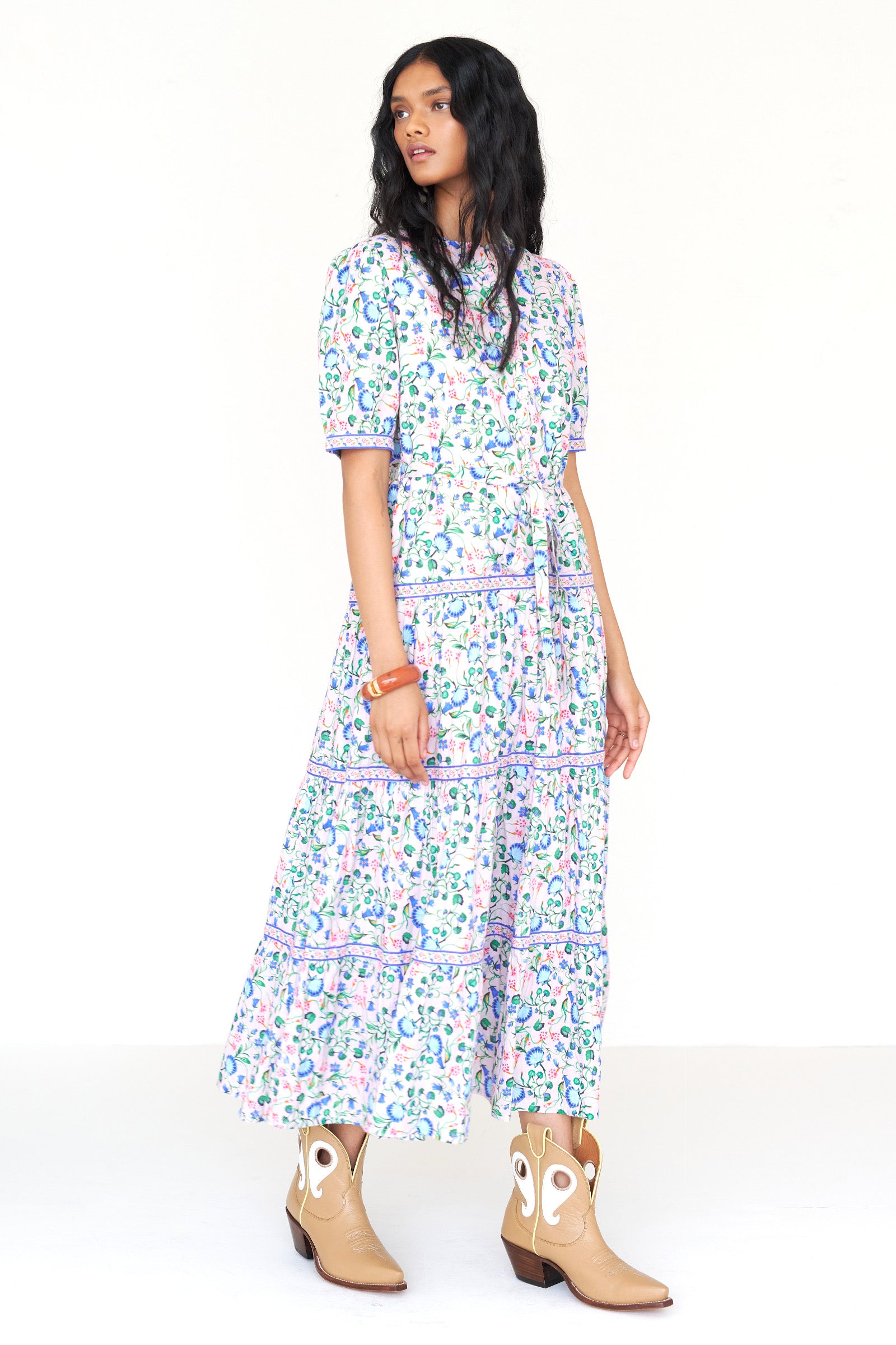 Front side view of a woman standing wearing the Saylor dress in Clam Garland print. It features a stand collar, contrast trim, tiered skirt, detachable belt, and full-length shirtdress silhouette.