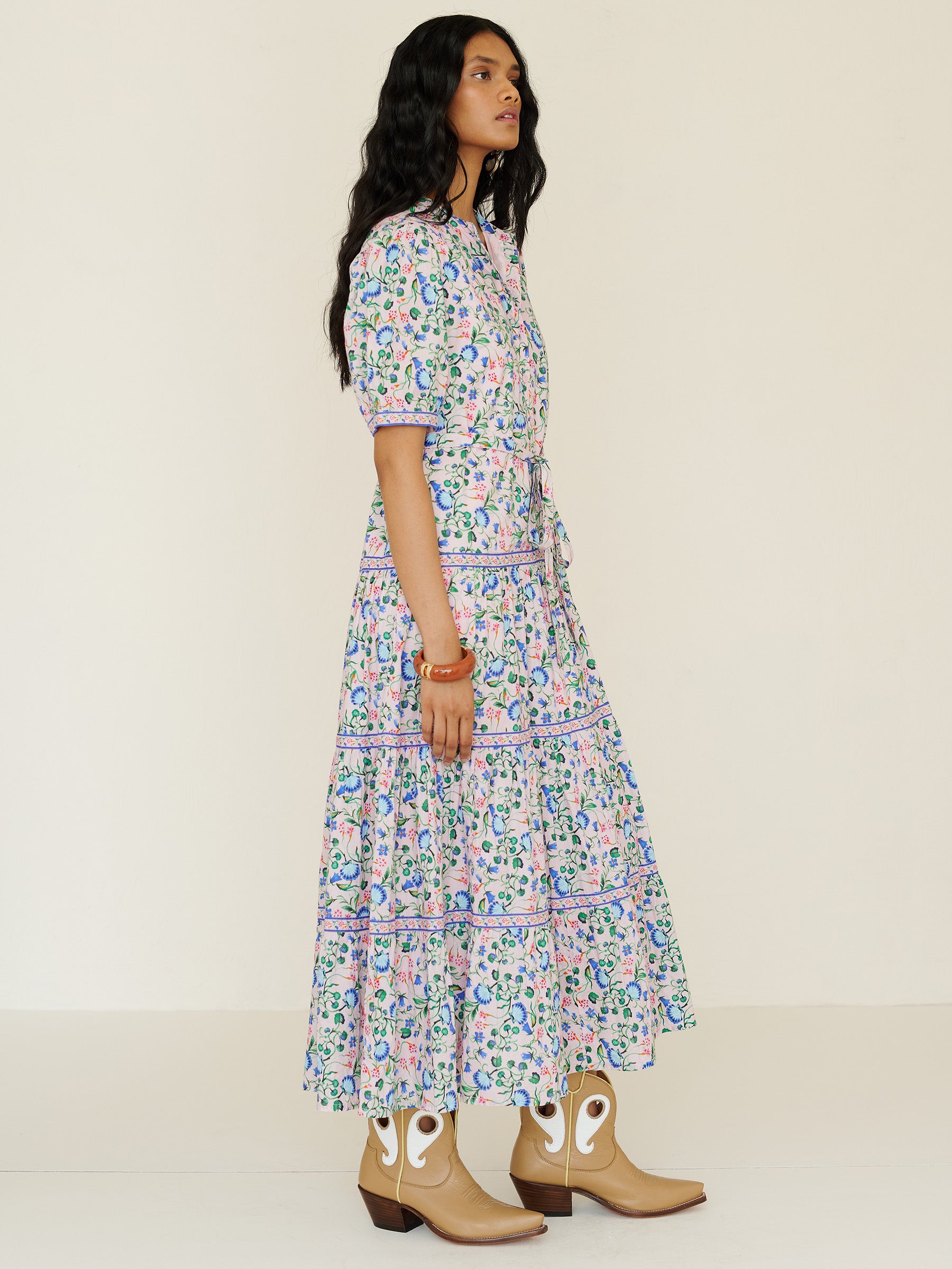 Side view of a woman standing. She is wearing the Saylor dress in Clam Garland floral print. It features a classic shirtdress design with stand collar, tiered skirt, contrast trim, and a detachable belt.