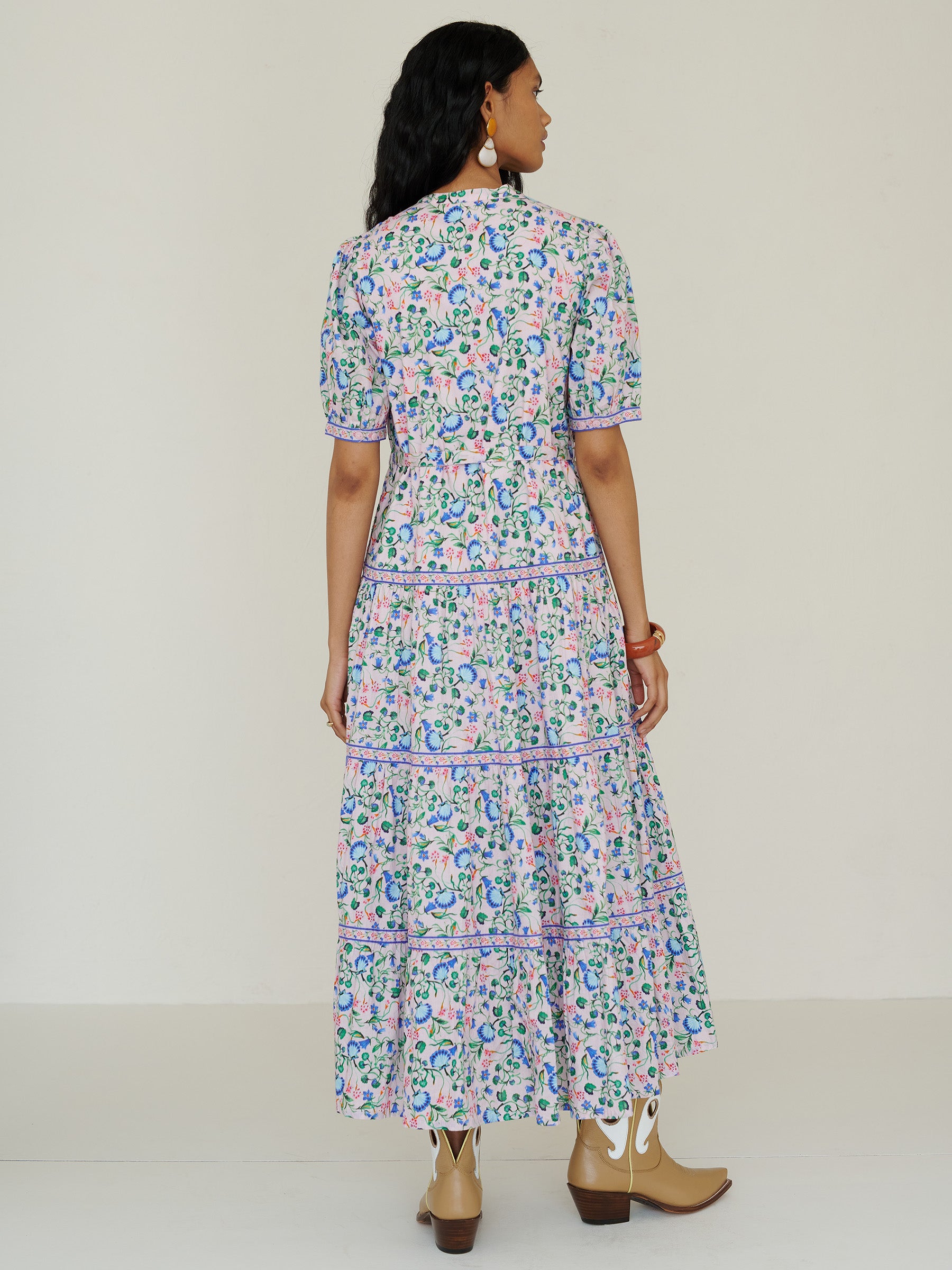 Back view of a woman standing. She is wearing the Saylor dress in Clam Garland floral print. It features a classic shirtdress design with stand collar, tiered skirt, contrast trim, and a detachable belt.