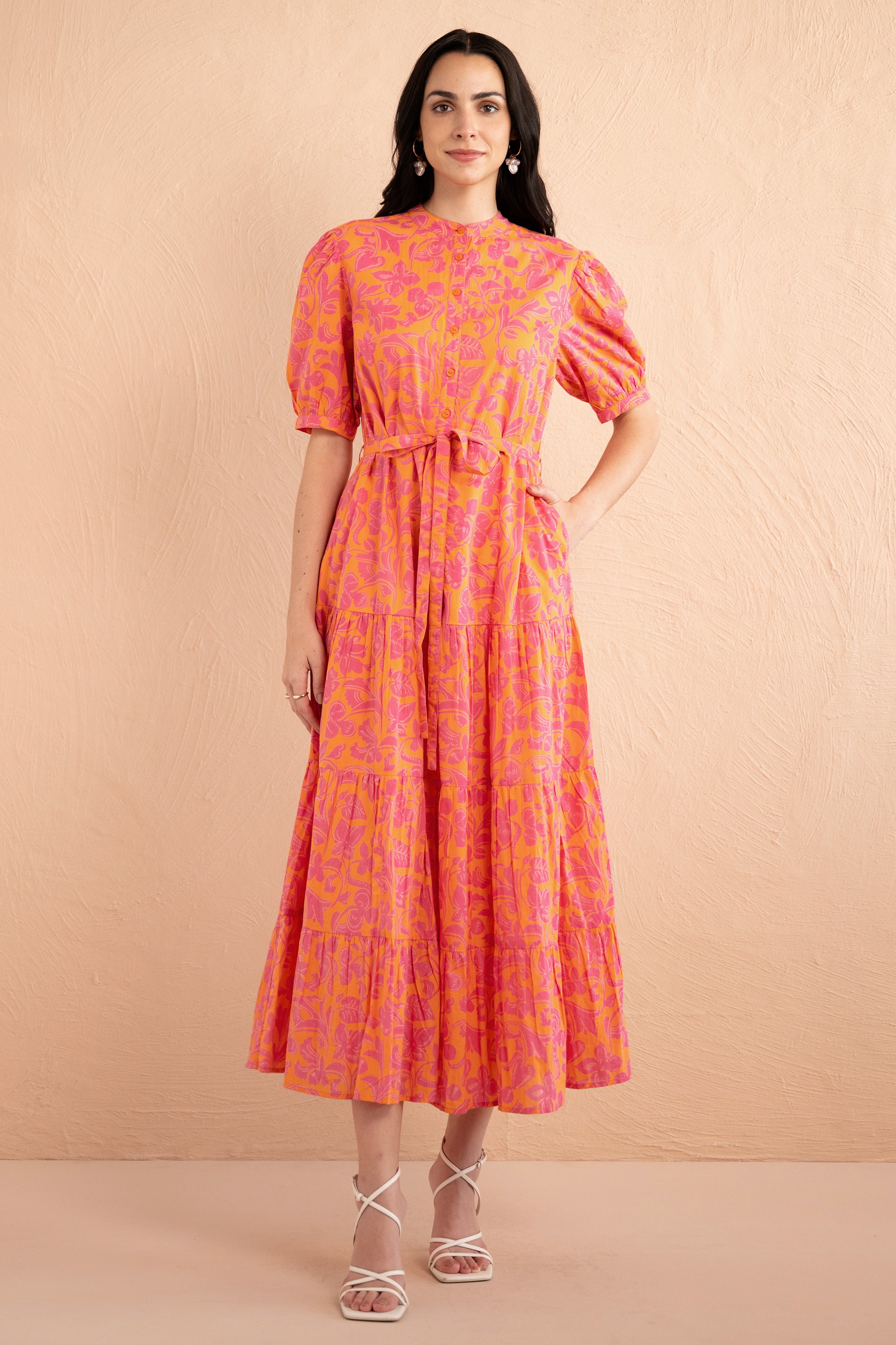 Front view of woman standing. She is wearing the Saylor Shirt dress in Gaia Nectarine print with sunset shades, featuring a tiered skirt, button front, and detachable belt.