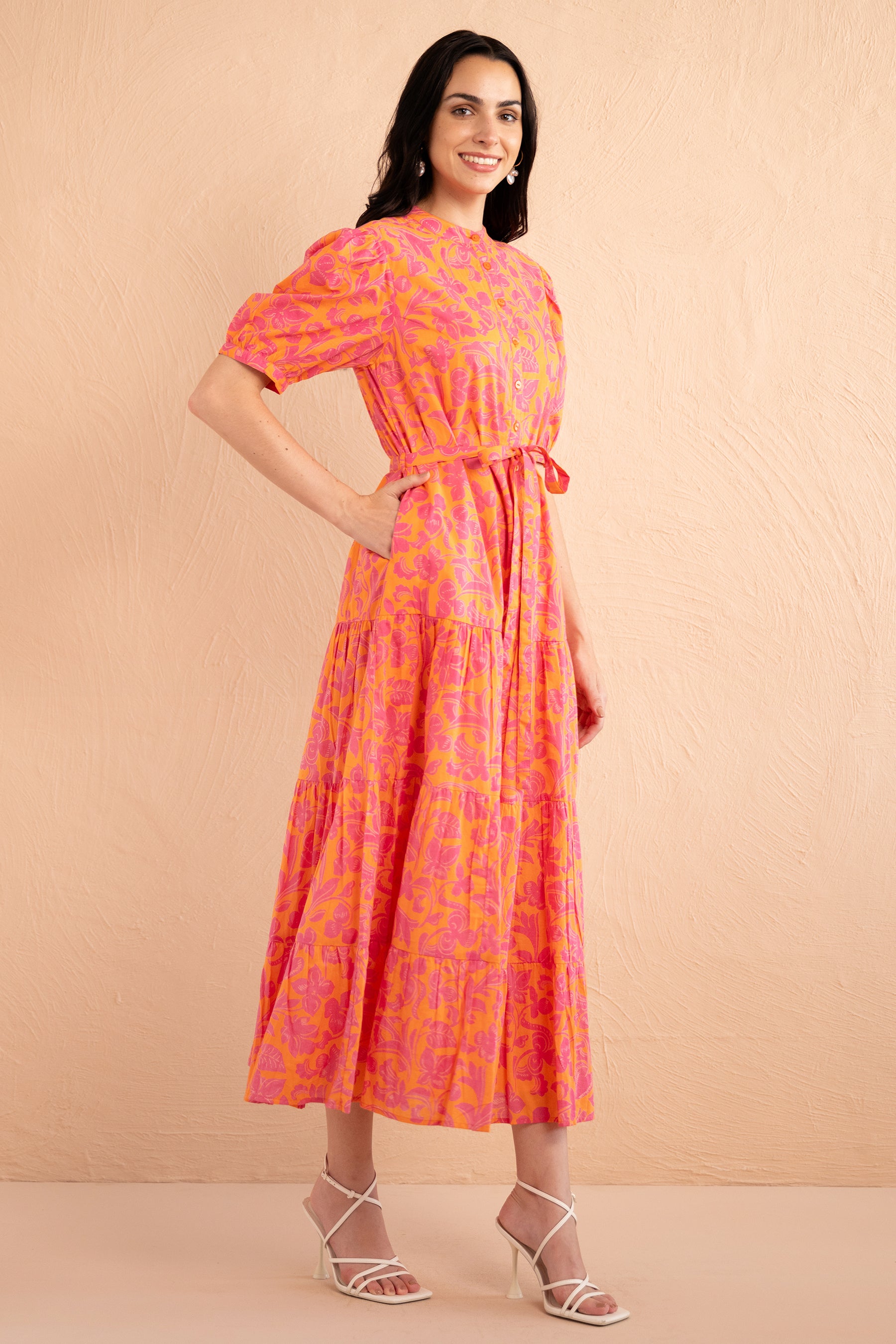 Side view of woman standing. She is wearing the Saylor Shirt dress in Gaia Nectarine print with sunset shades, featuring a tiered skirt, button front, and detachable belt.