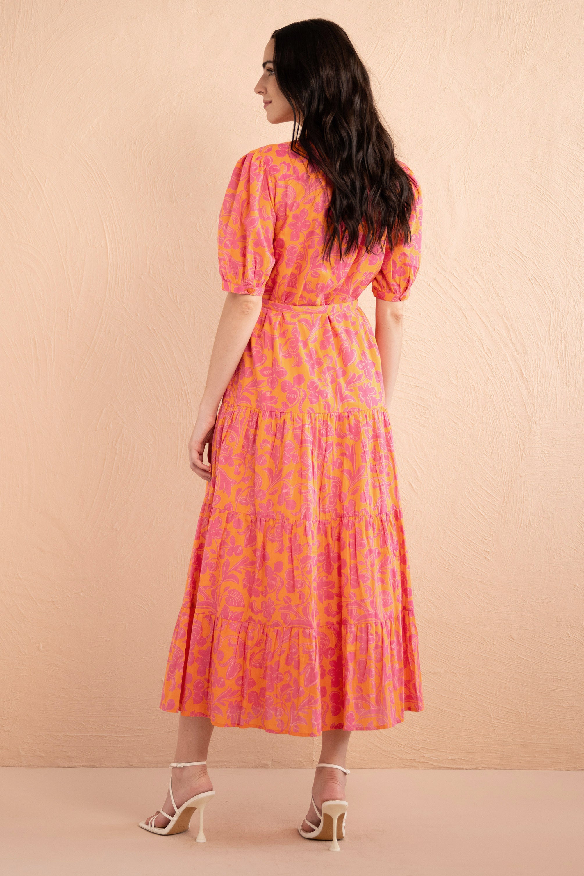 Back view of woman standing. She is wearing the Saylor Shirt dress in Gaia Nectarine print with sunset shades, featuring a tiered skirt, button front, and detachable belt.