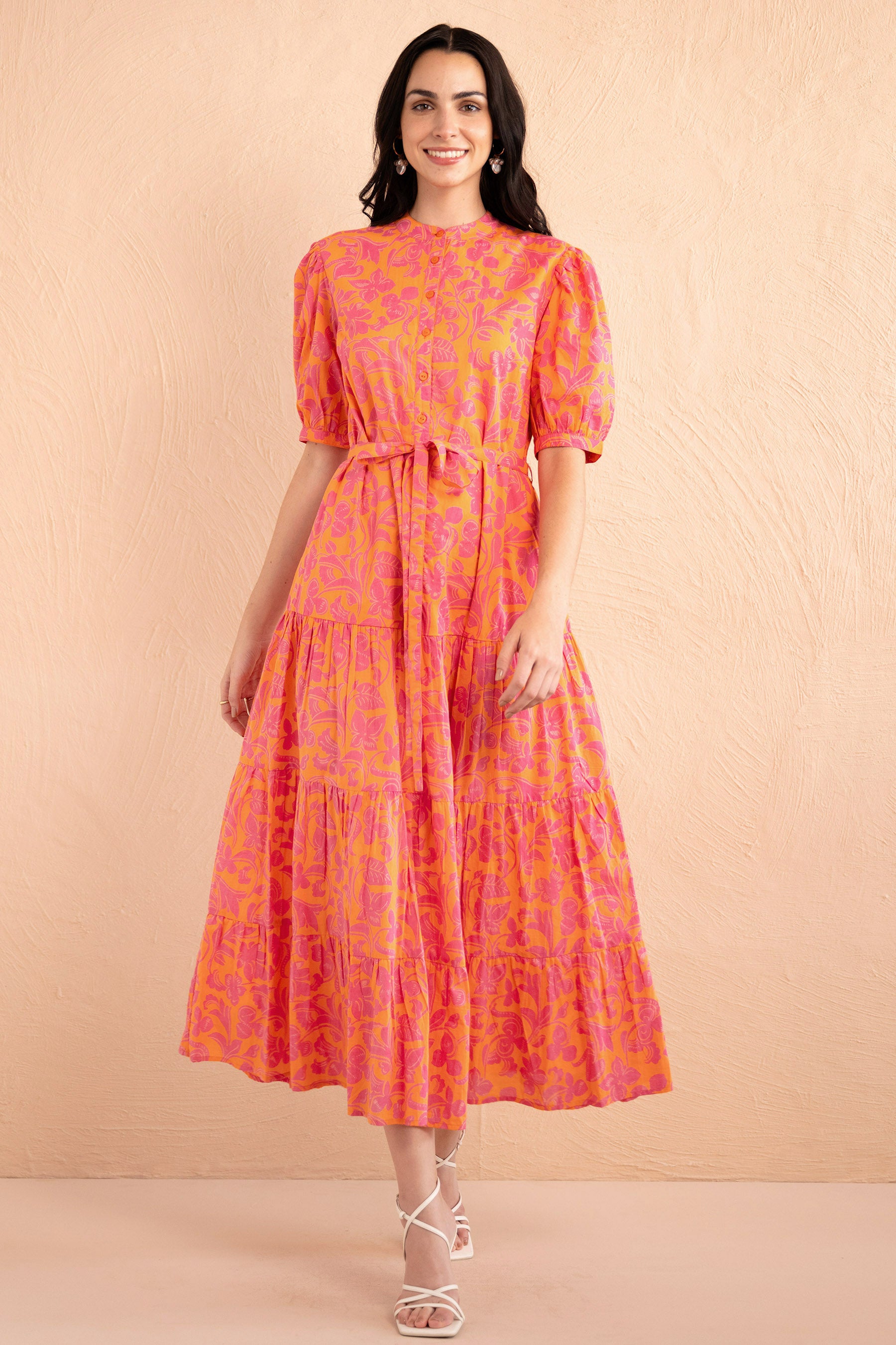 Front view of woman walking. She is wearing the Saylor Shirt dress in Gaia Nectarine print with sunset shades, featuring a tiered skirt, button front, and detachable belt.