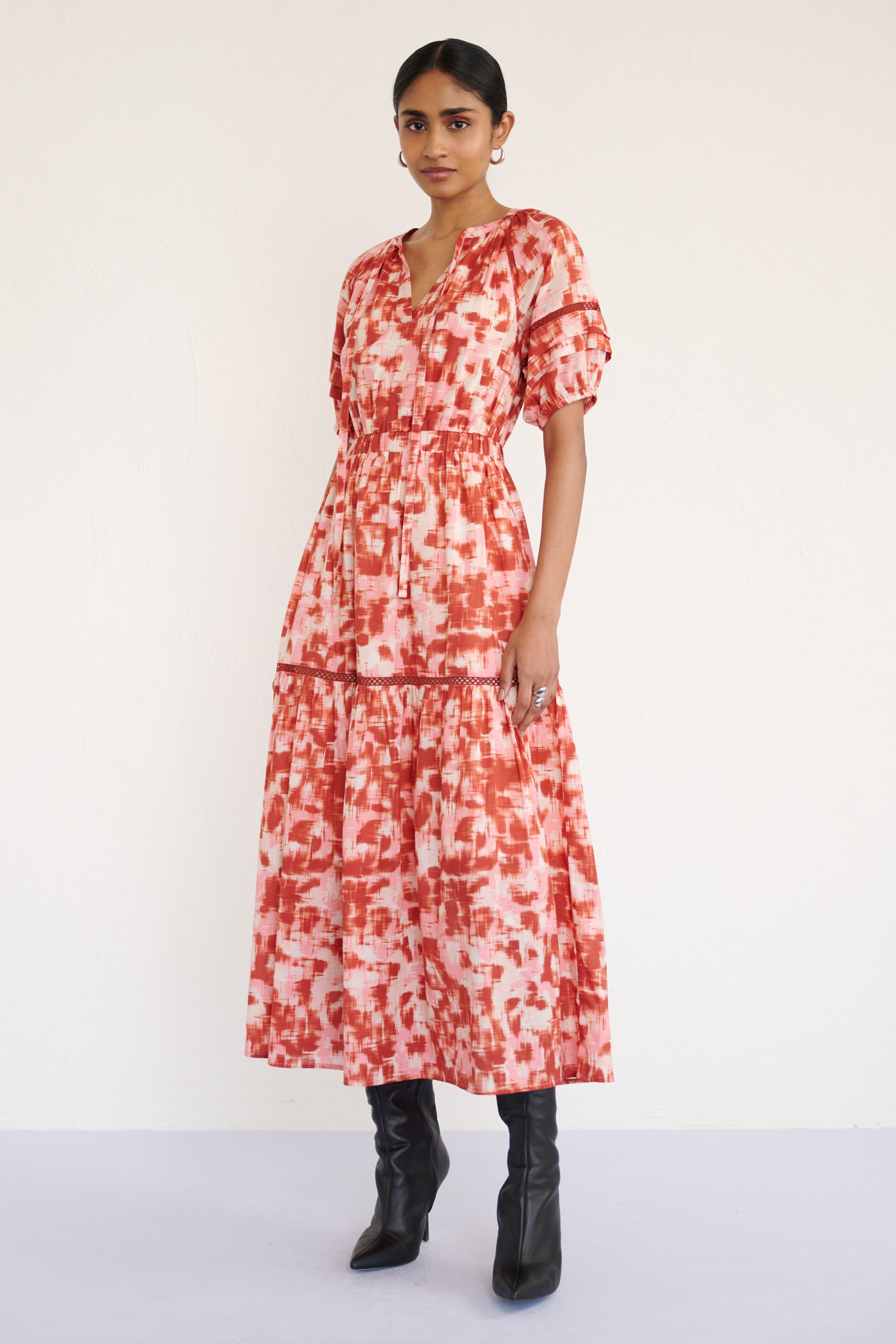 Front view of woman posing. She is wearing Selma Dress in Amur print, Honey color. It is a full-length V-neck dress with tie-neck detail, lace inserts on the skirt and sleeves, and an ikat-inspired animal print.