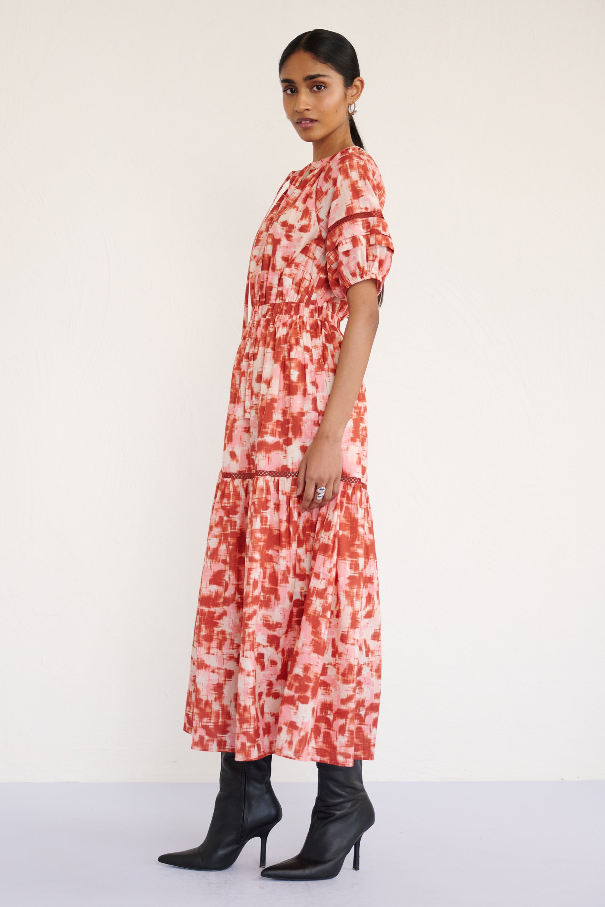 Side view of woman wearing a full-length V-neck dress with tie-neck detail, lace inserts on the skirt and sleeves, and an ikat-inspired animal print.
