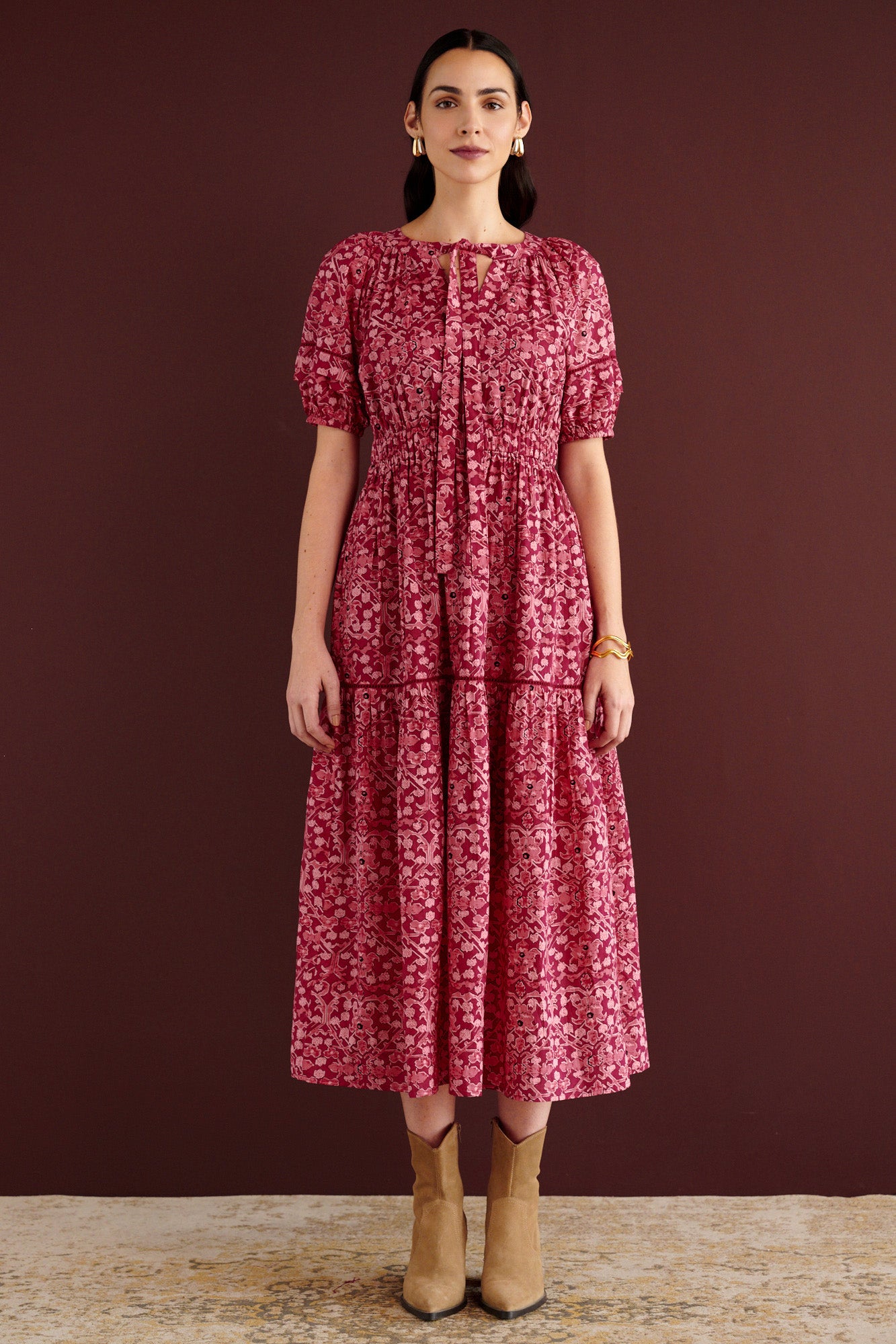 Front view of woman standing. She is wearing the Selma full-length V-neck dress in Ottoman print, with tie-neck, elastic waist, lace insets at skirt and sleeves, smooth cotton cambric, side-seam pockets, and fully lined construction.