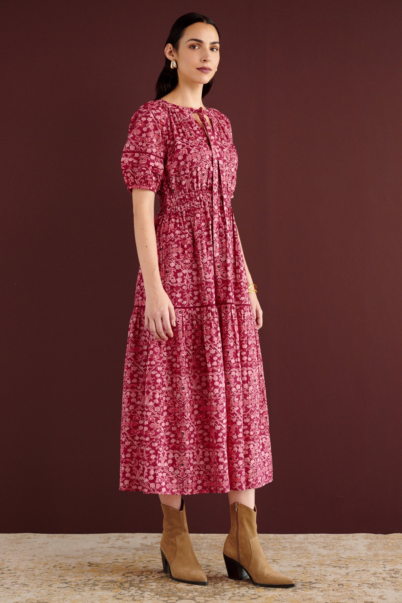 Side view of woman standing. She is wearing the Selma full-length V-neck dress in Ottoman print, with tie-neck, elastic waist, lace insets at skirt and sleeves, smooth cotton cambric, side-seam pockets, and fully lined construction.