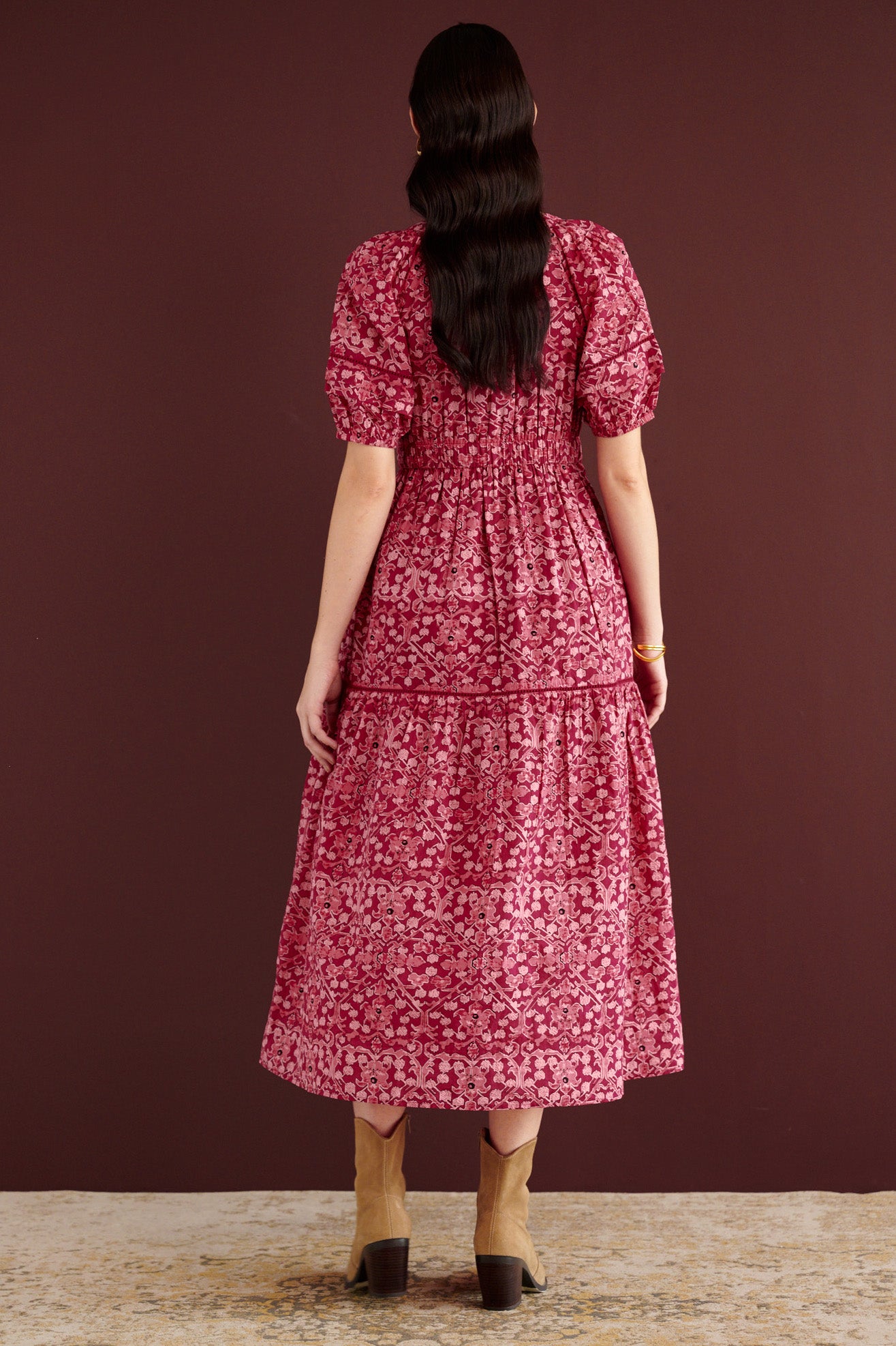 Back view of woman standing. She is wearing the Selma full-length V-neck dress in Ottoman print, with tie-neck, elastic waist, lace insets at skirt and sleeves, smooth cotton cambric, side-seam pockets, and fully lined construction.
