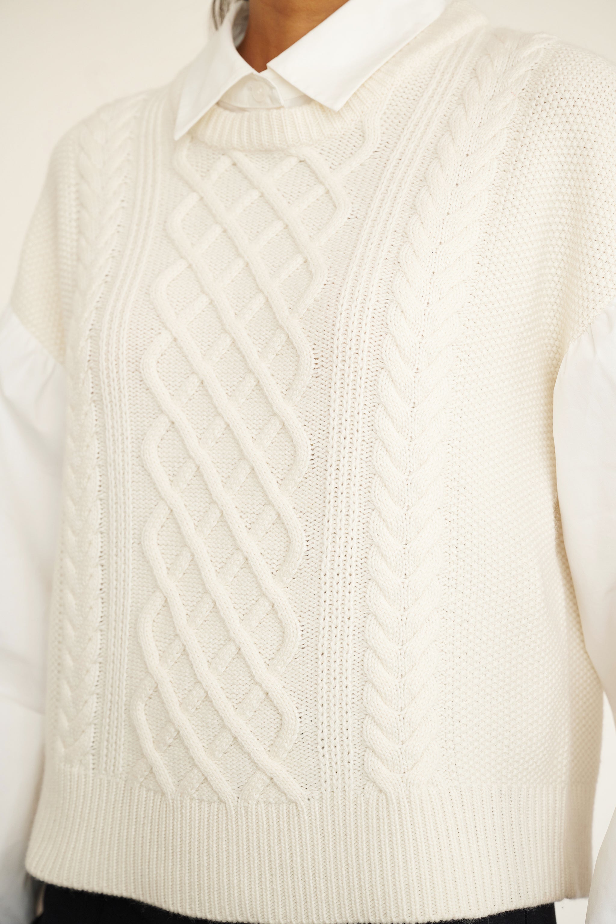 Front view close up of woman wearing a cable knit sweater with poplin shirt collar and sleeves, featuring elastic cuffs for shape and a layered look.