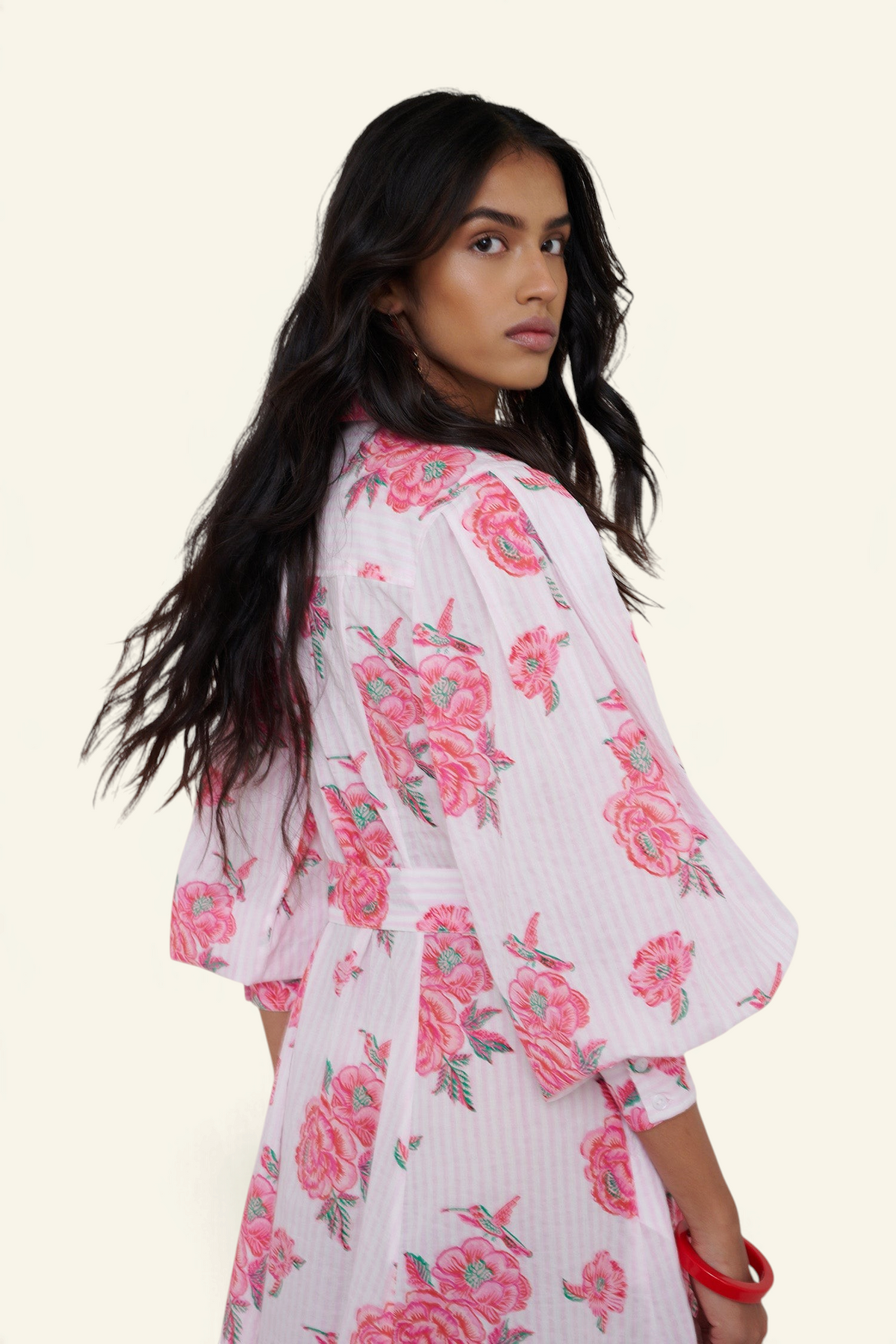 Woman wearing a white kimono-style garment with pink floral patterns on a plain background