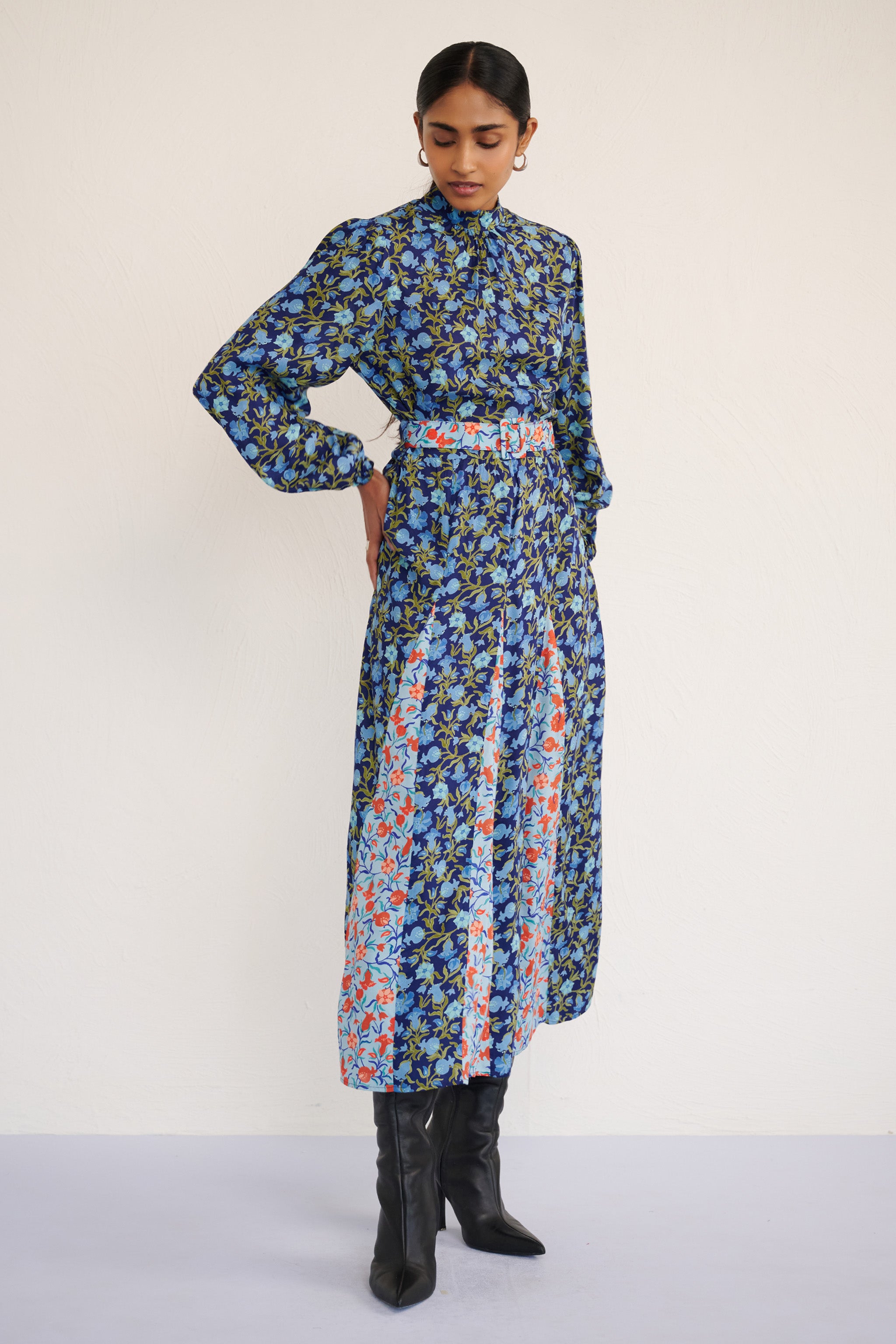 Front view of woman wearing a full-length dress with a stand collar, fitted waist belt, and flowing skirt featuring contrast print inserts and a pomegranate vine motif.